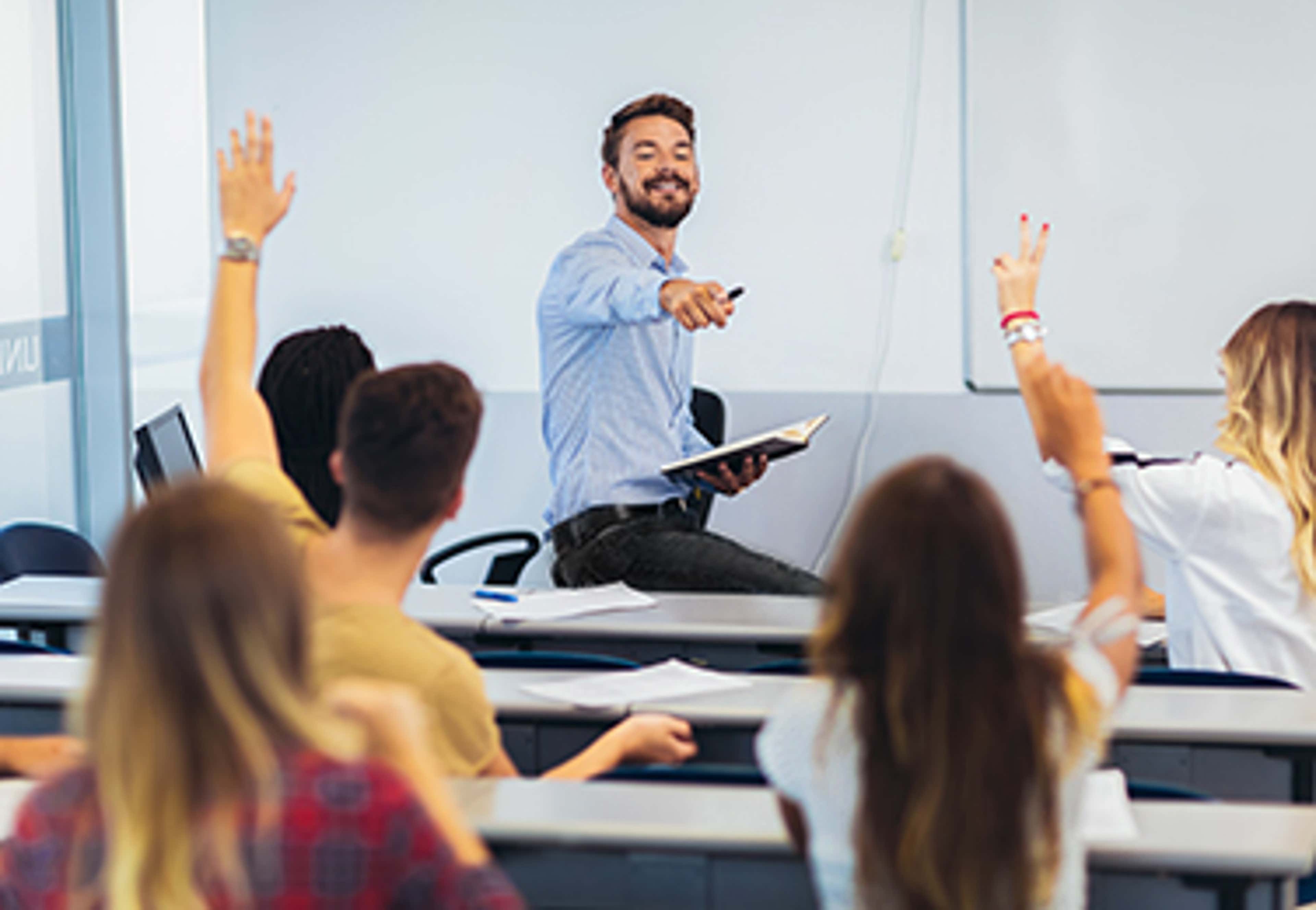 Teacher at front of room of students with hands up