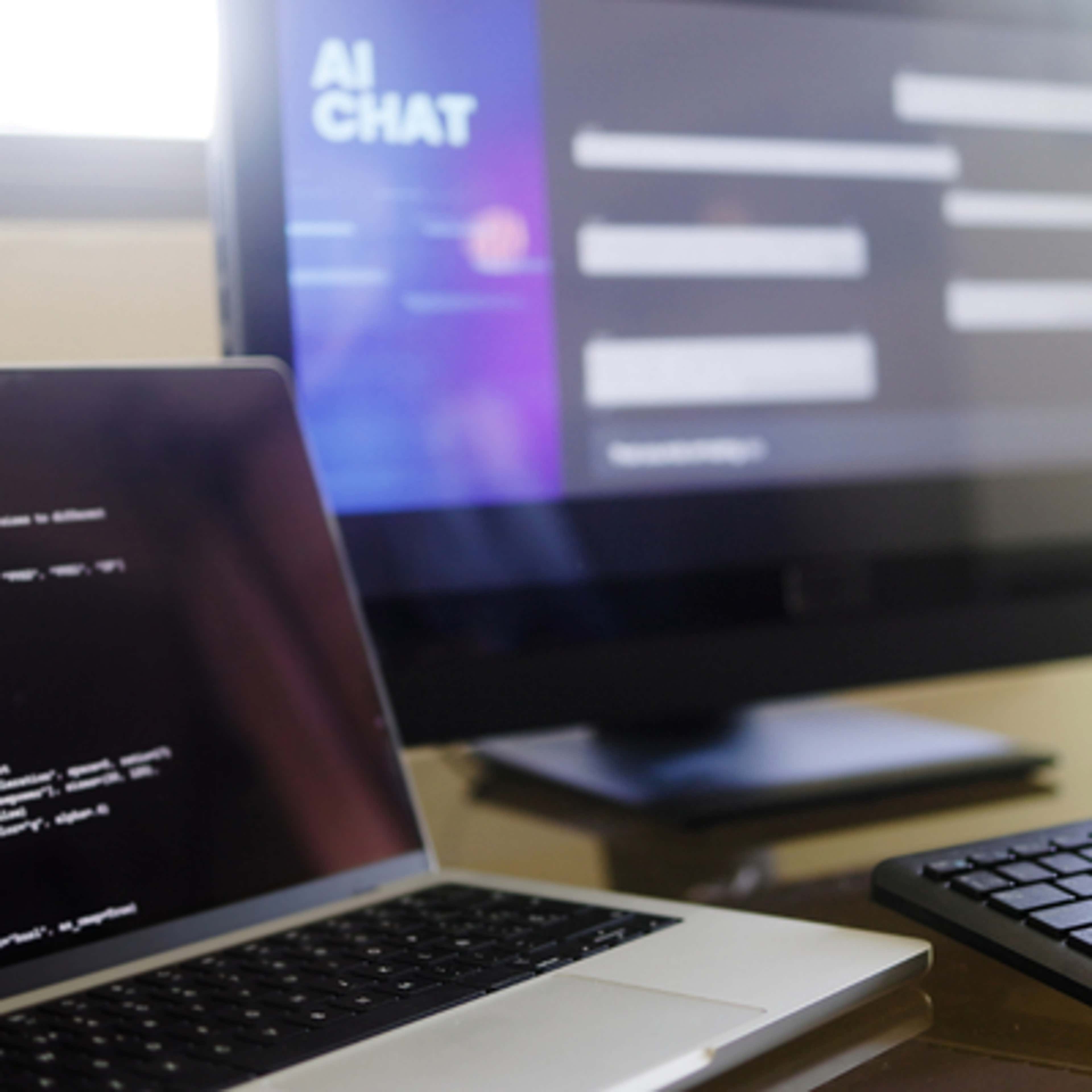 A desk displays a laptop, keyboard, and monitor, illustrating a modern office environment.