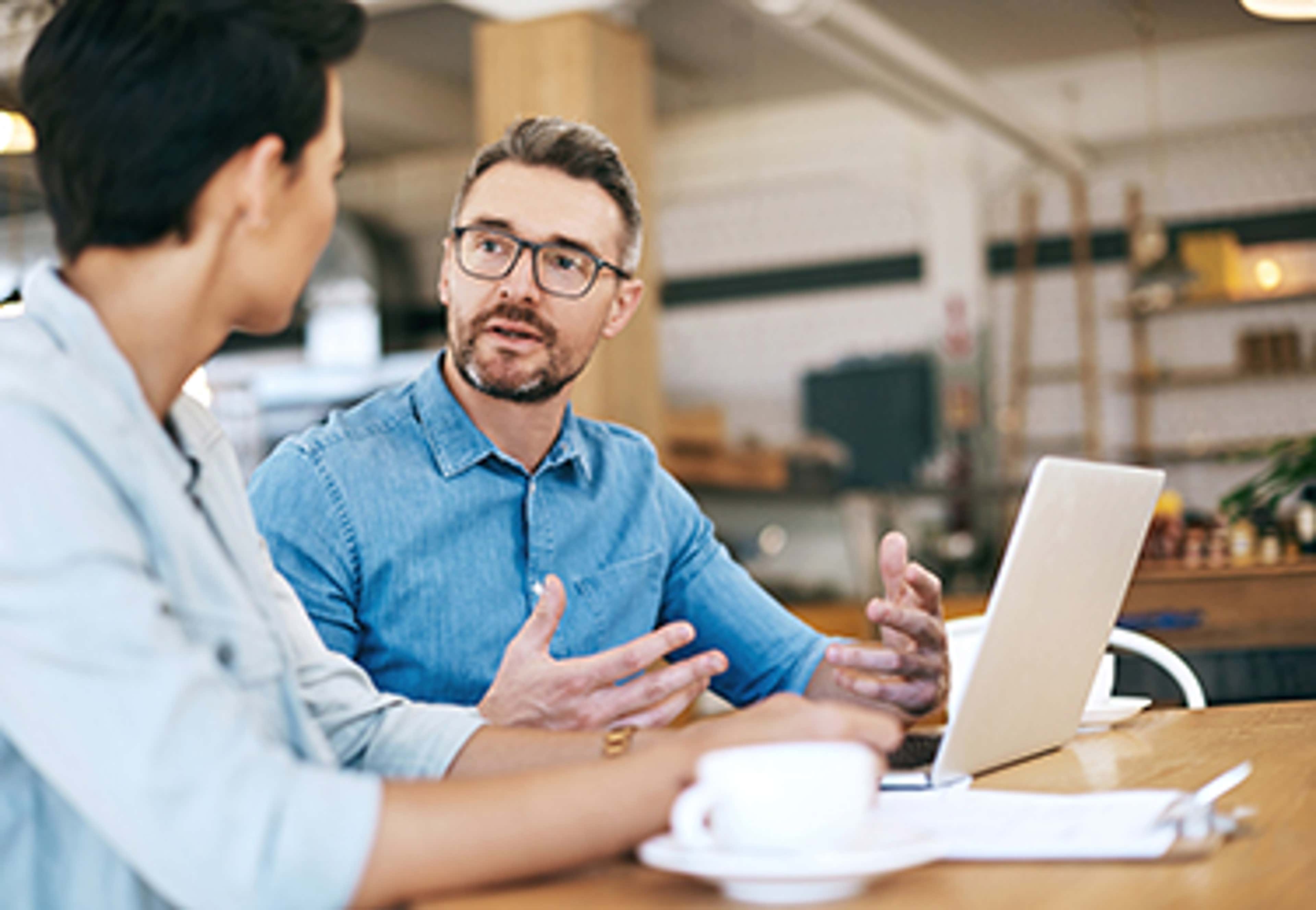 Man and woman in shop talking at table with laptop