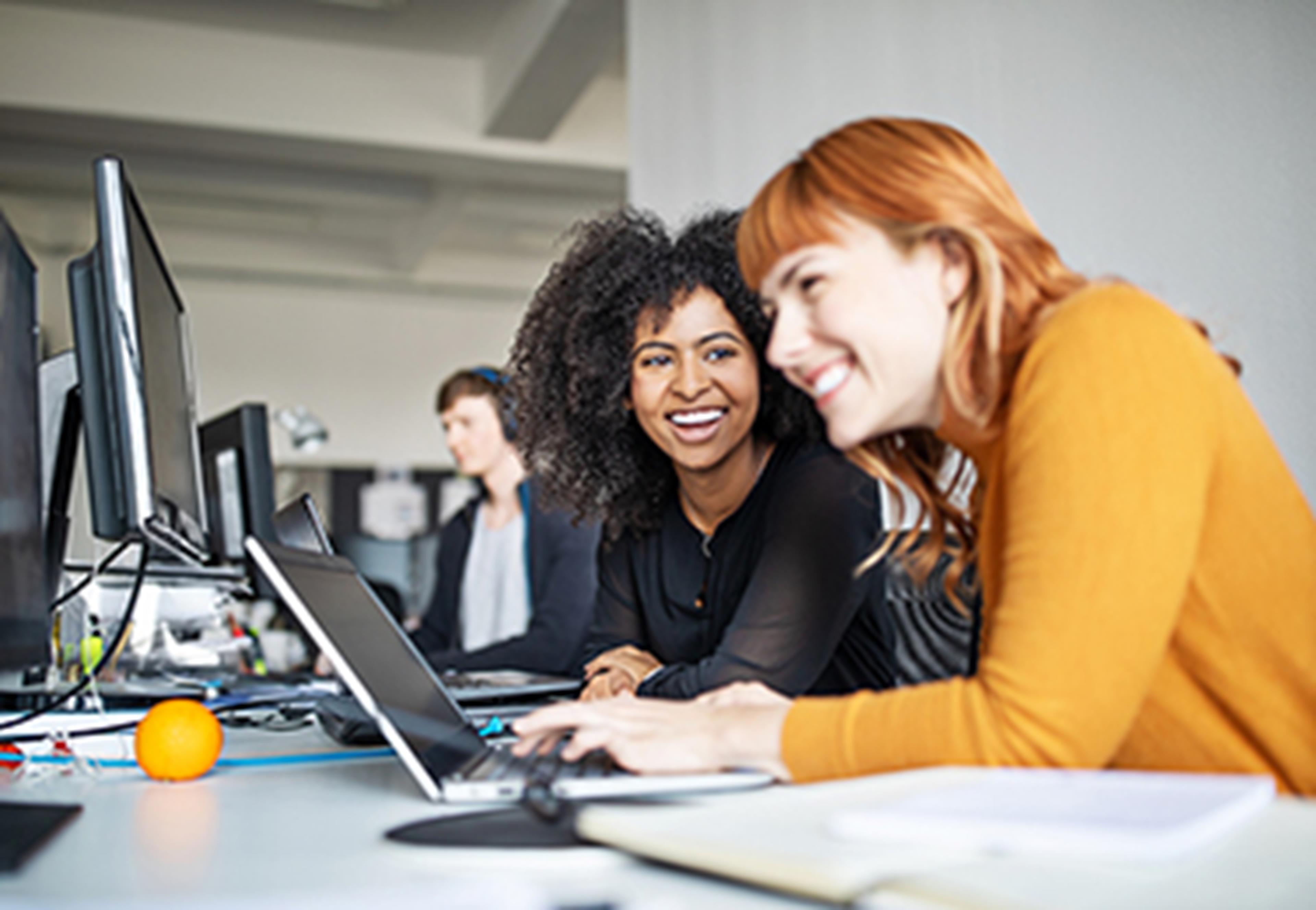 Two women at desk with laptop laughing