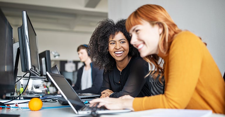 Two women at desk with laptop laughing