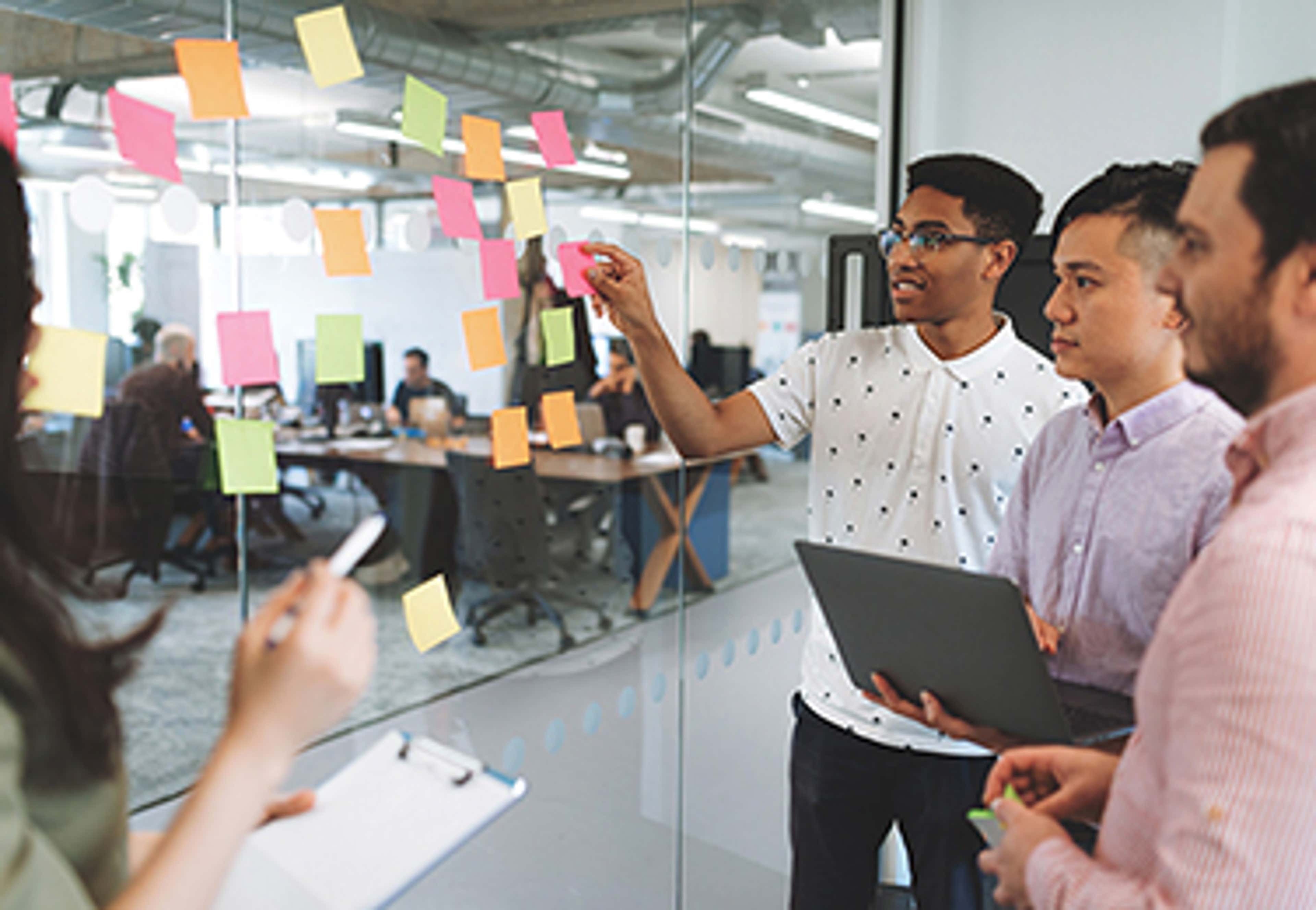 4 people standing at glass wall with sticky notes