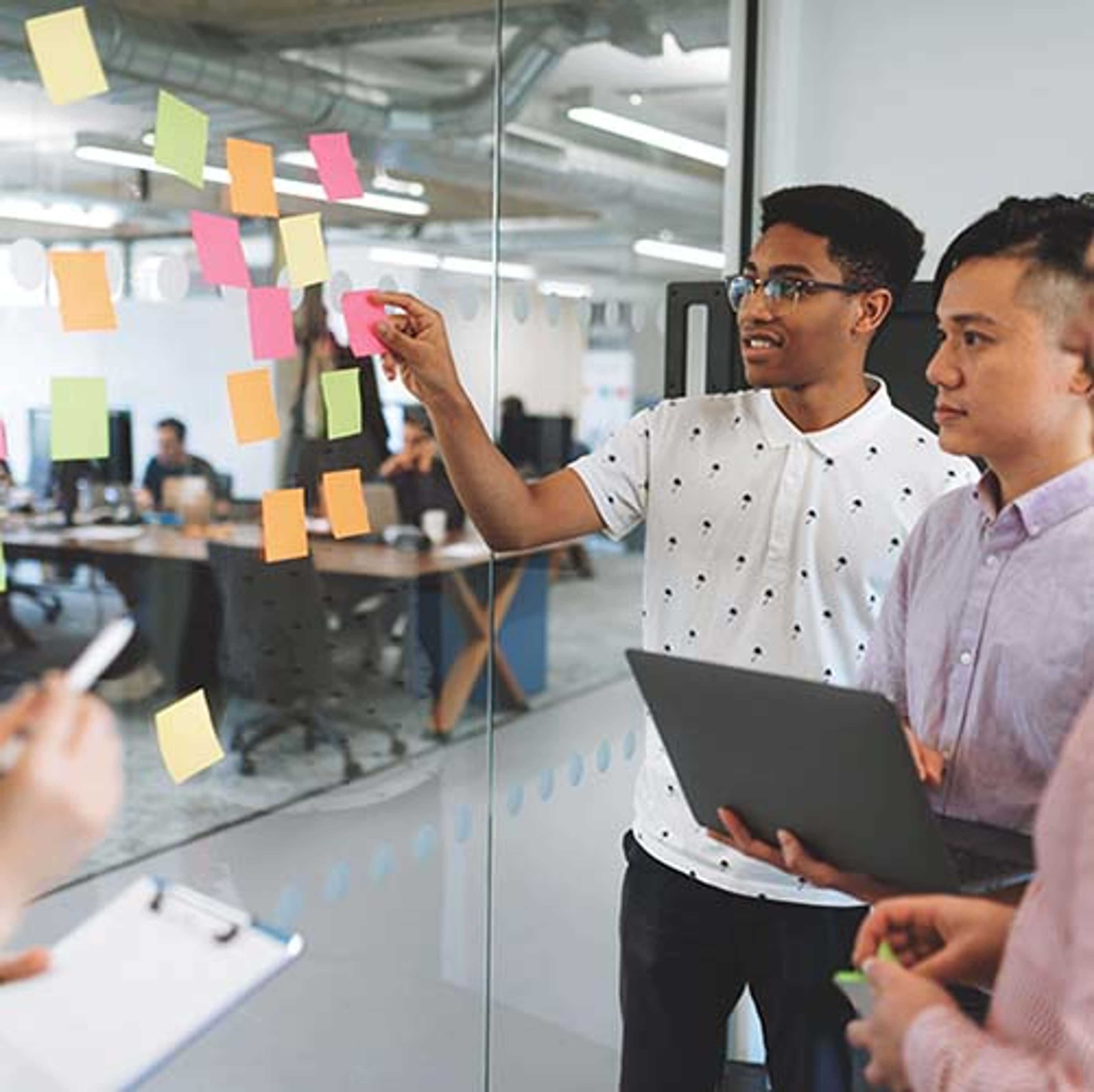 4 people standing at glass wall with sticky notes