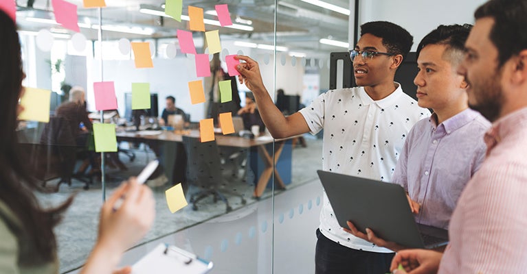 4 people standing at glass wall with sticky notes