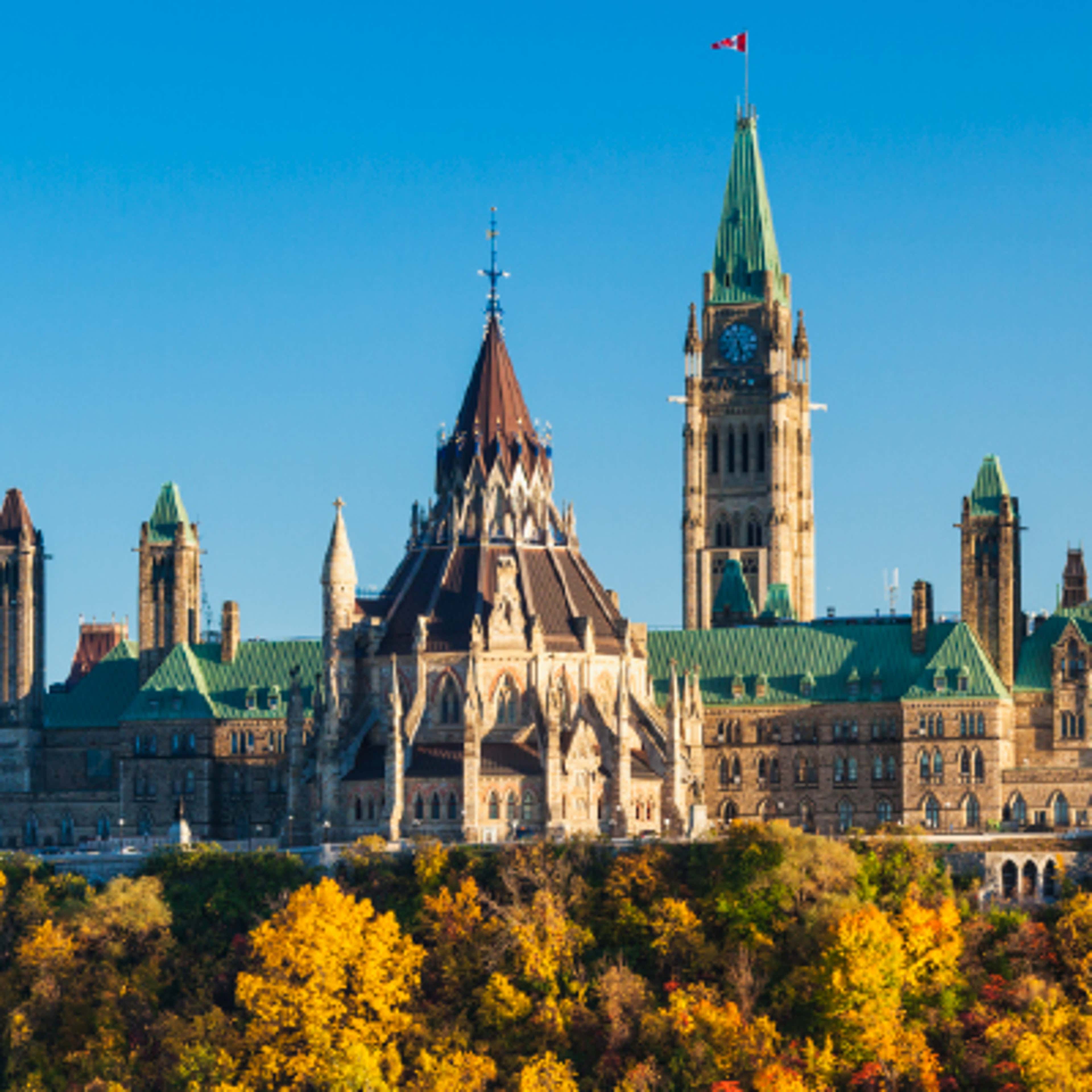 The historic Parliament Building in Ottawa, Canada, with its grand facade and prominent clock tower amidst vibrant gardens.