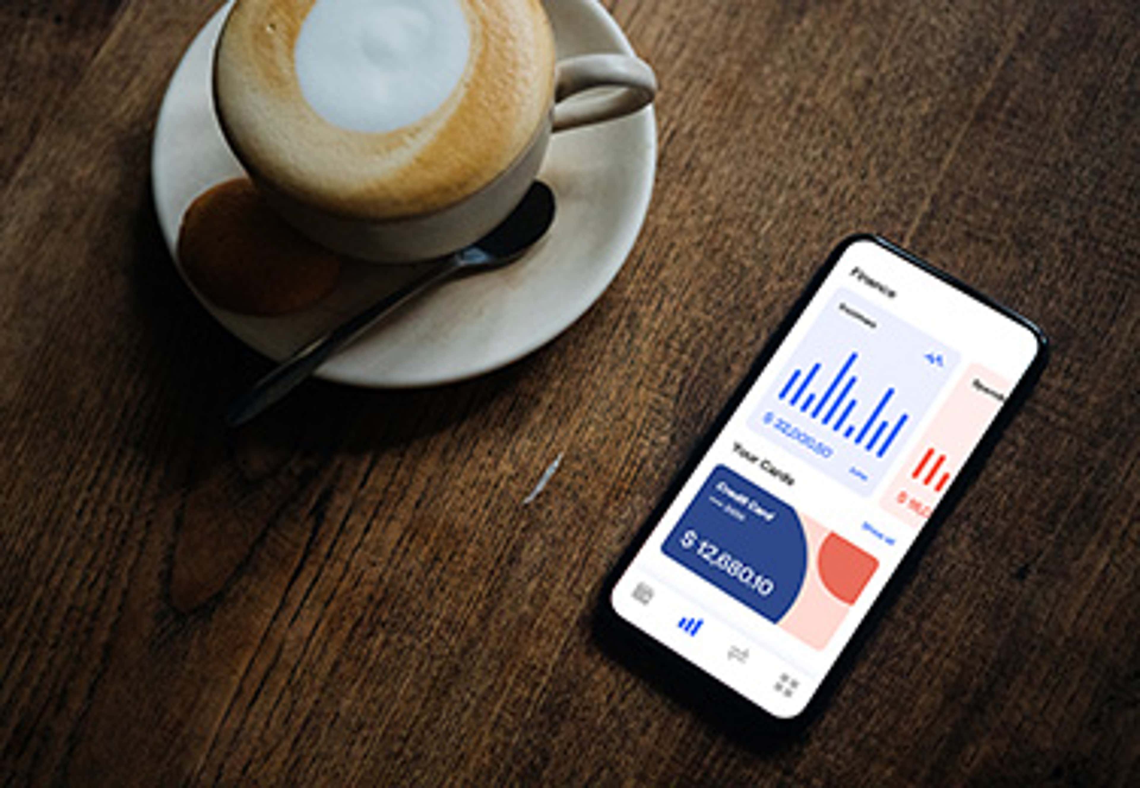 Cell phone with money app open on wood table with cup of coffee