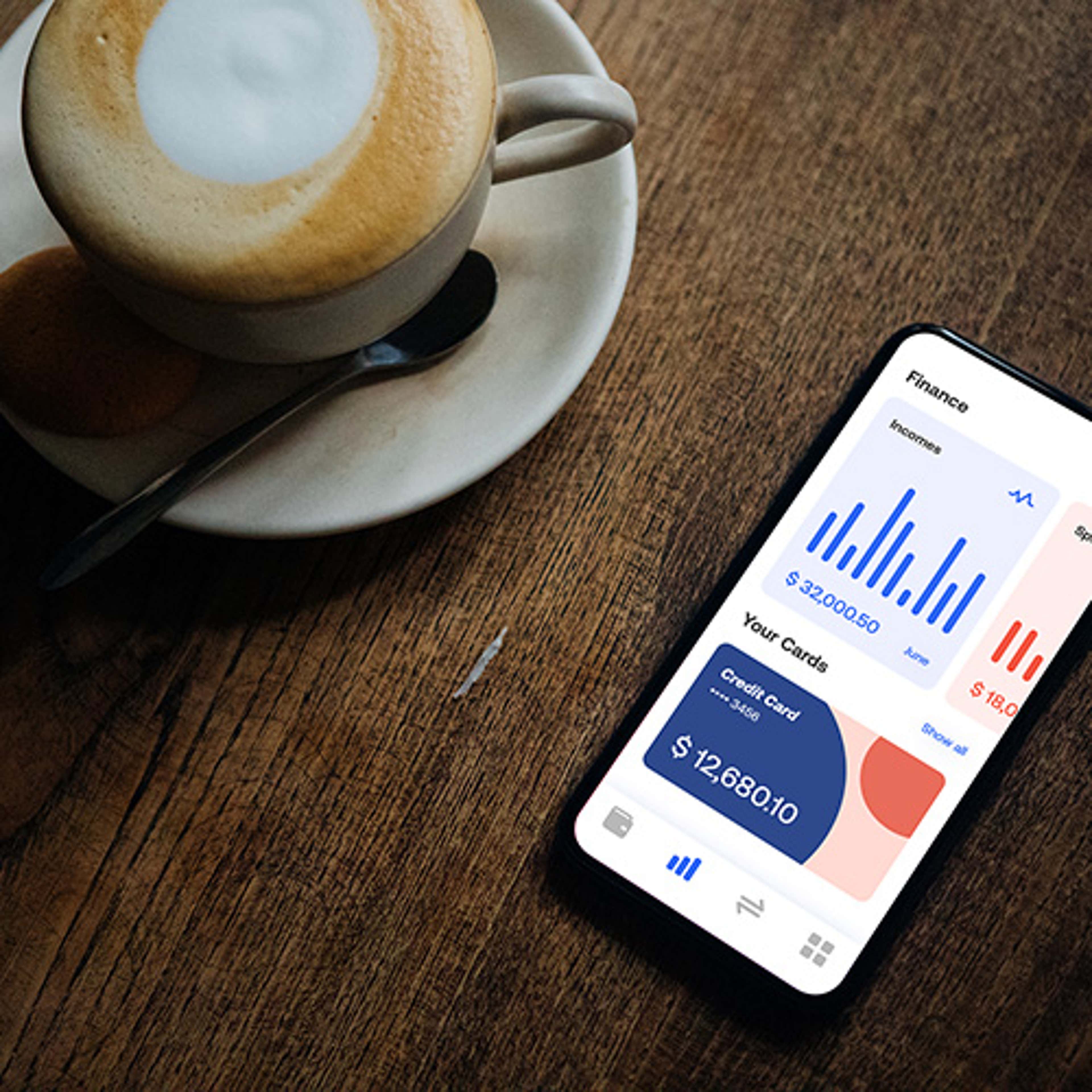 Cell phone with money app open on wood table with cup of coffee