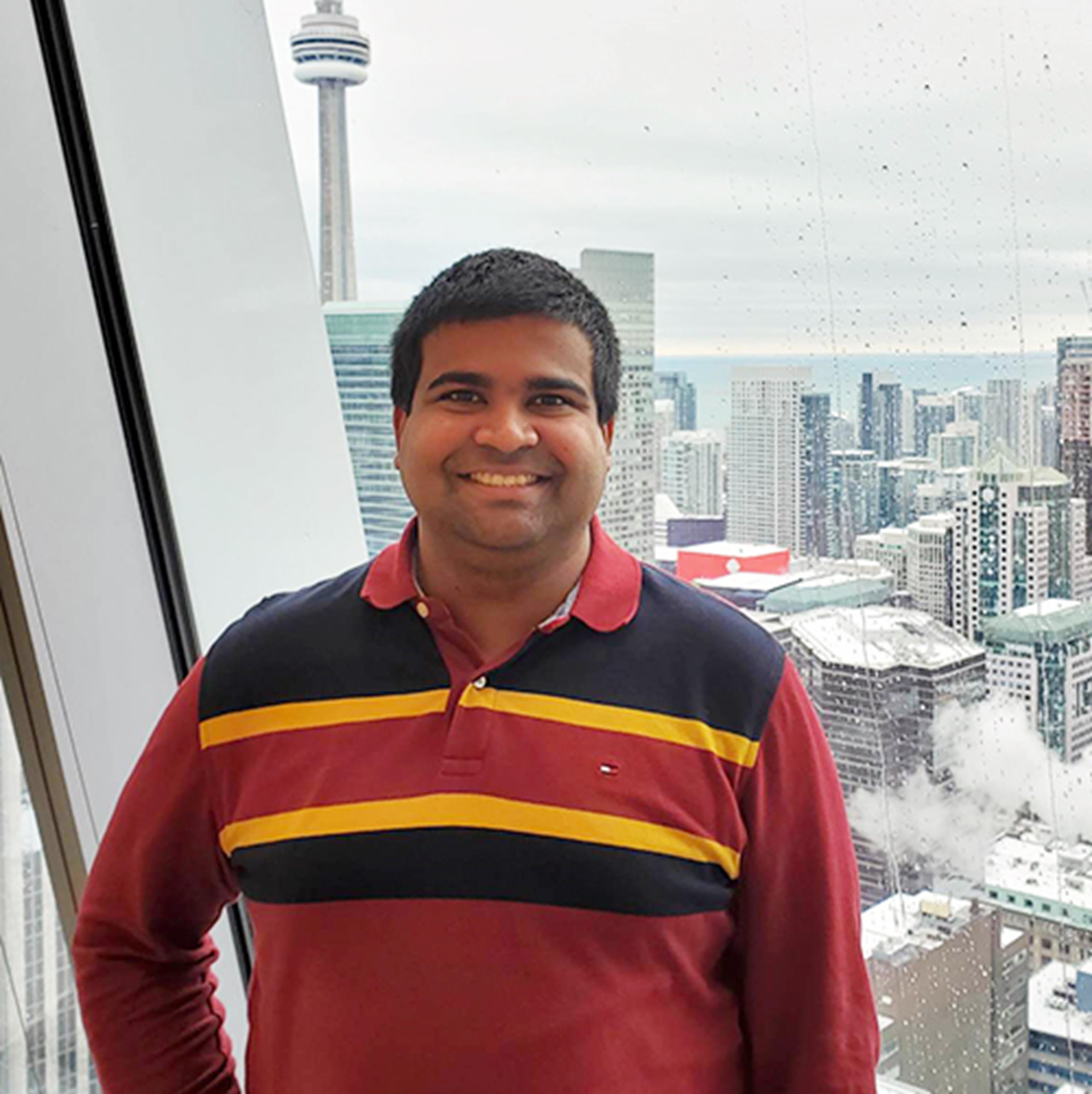 Dilshan in front of high rise building window with CN Tower and city buildings in the background