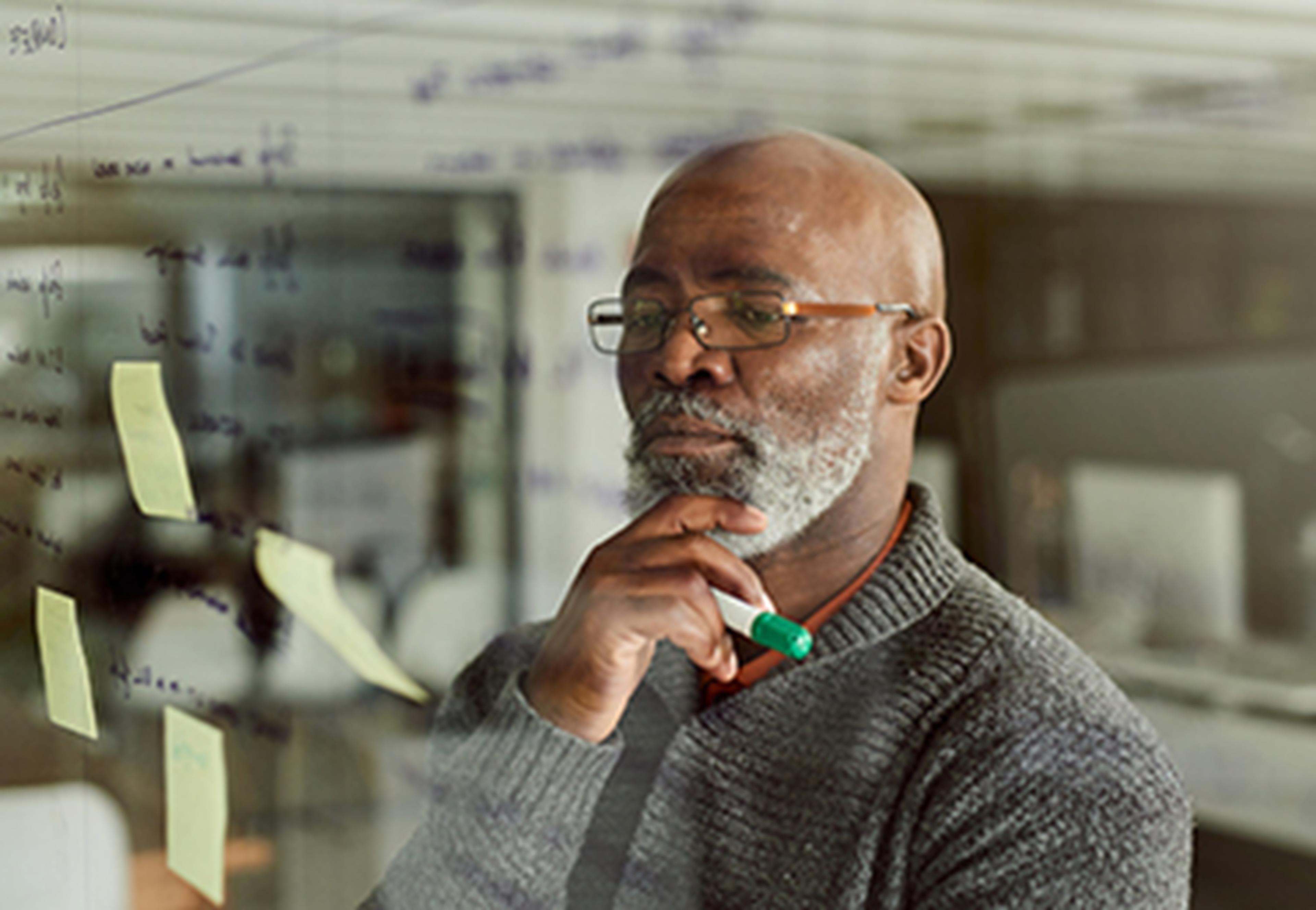 Man looking at glass board with writing on it