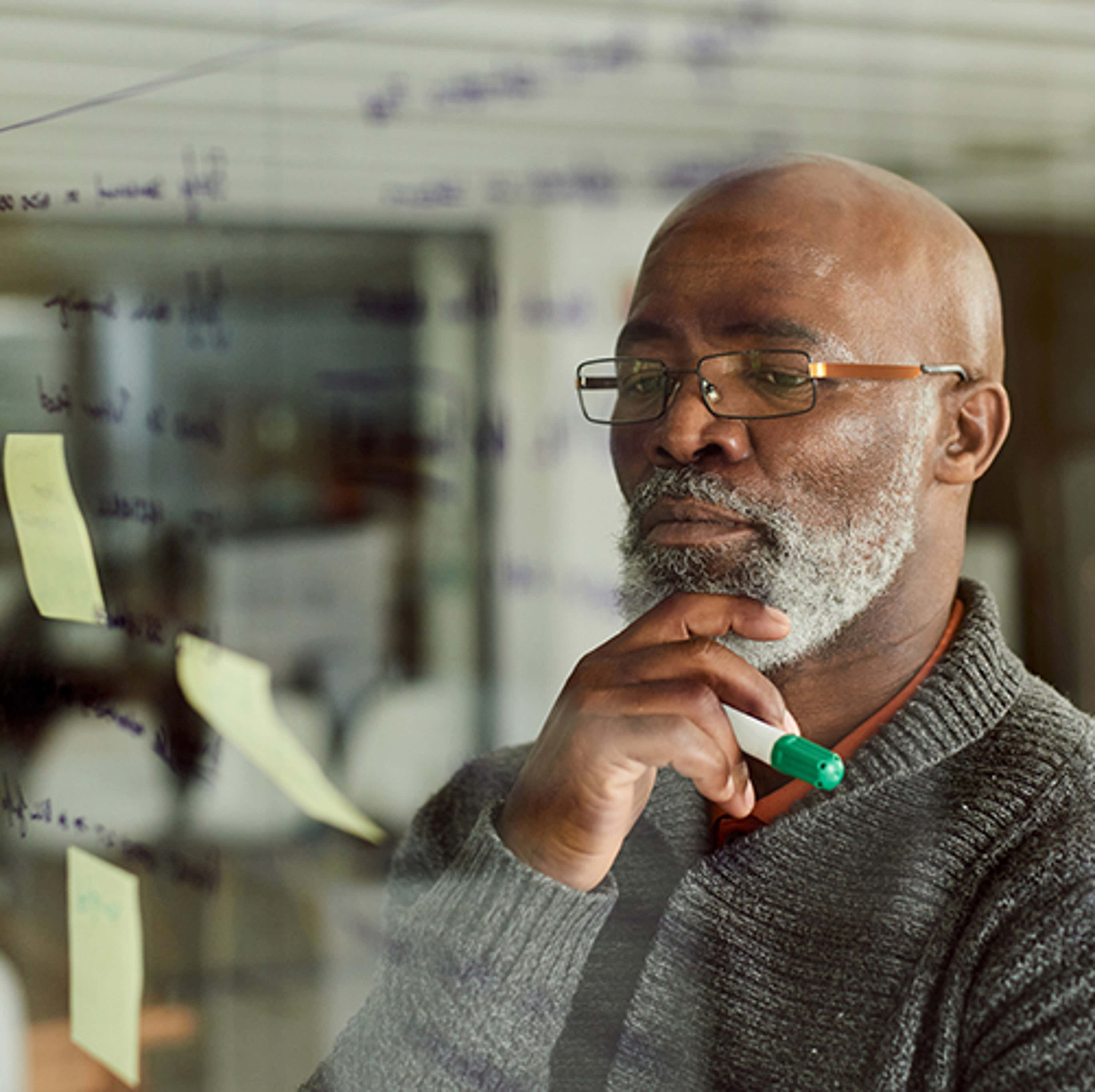 Man with beard looking at glass wall with writing and post-it notes