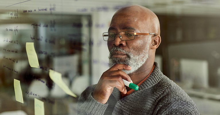 Man with beard looking at glass wall with writing and post-it notes