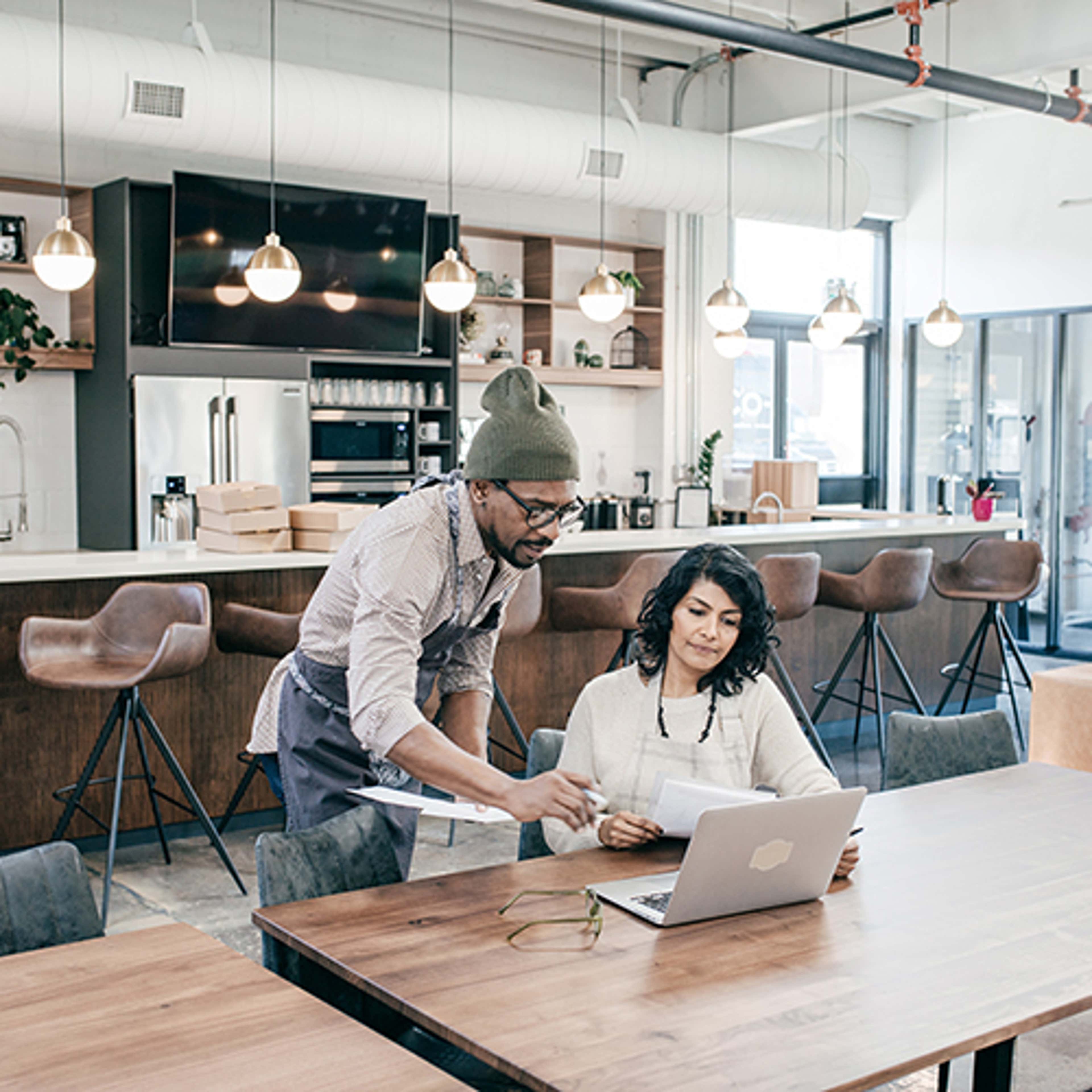 Two people sitting at table in cafe looking at laptop
