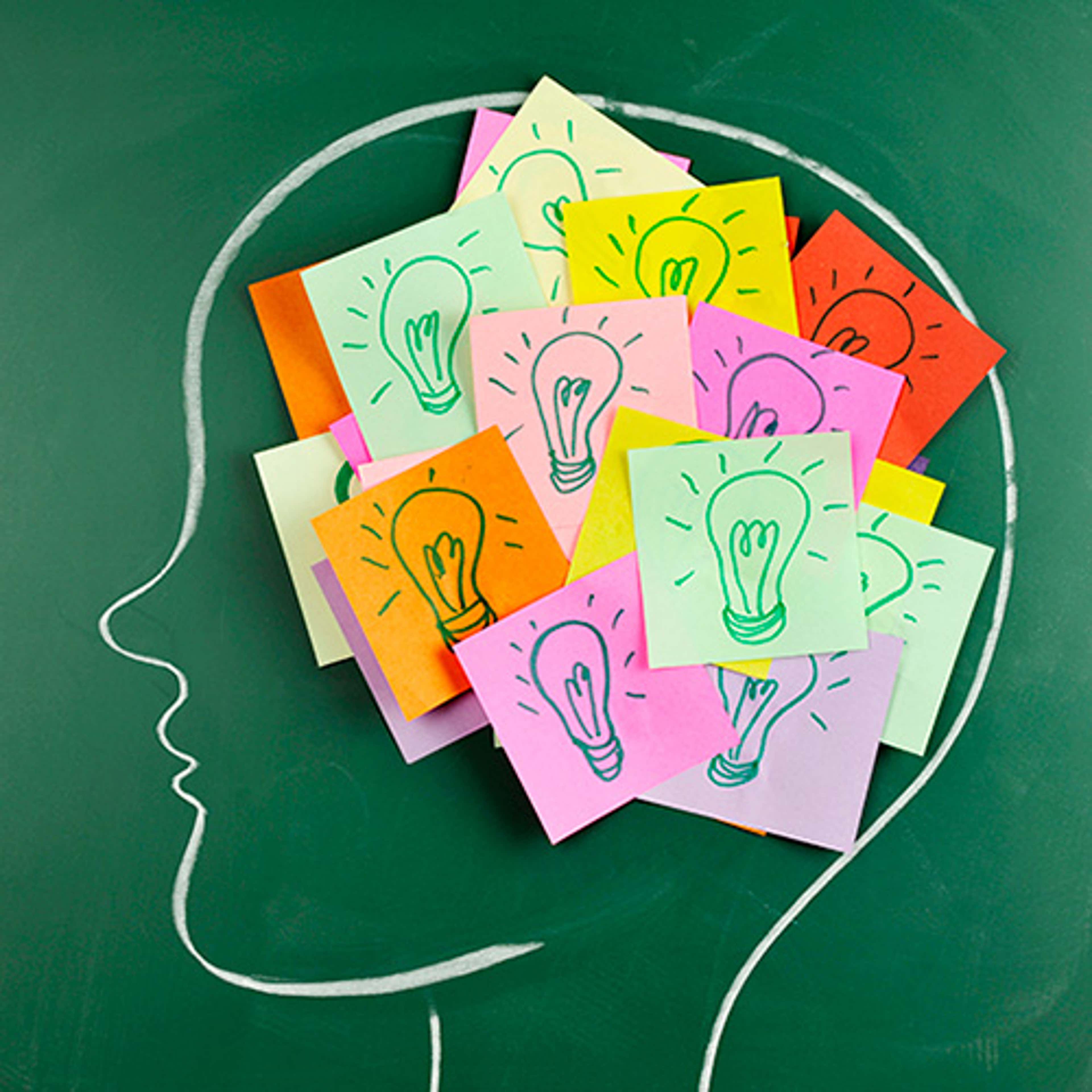 Head drawn in white chalk on a green chalkboard with post-it notes with lightbulbs drawn on them placed within the head.
