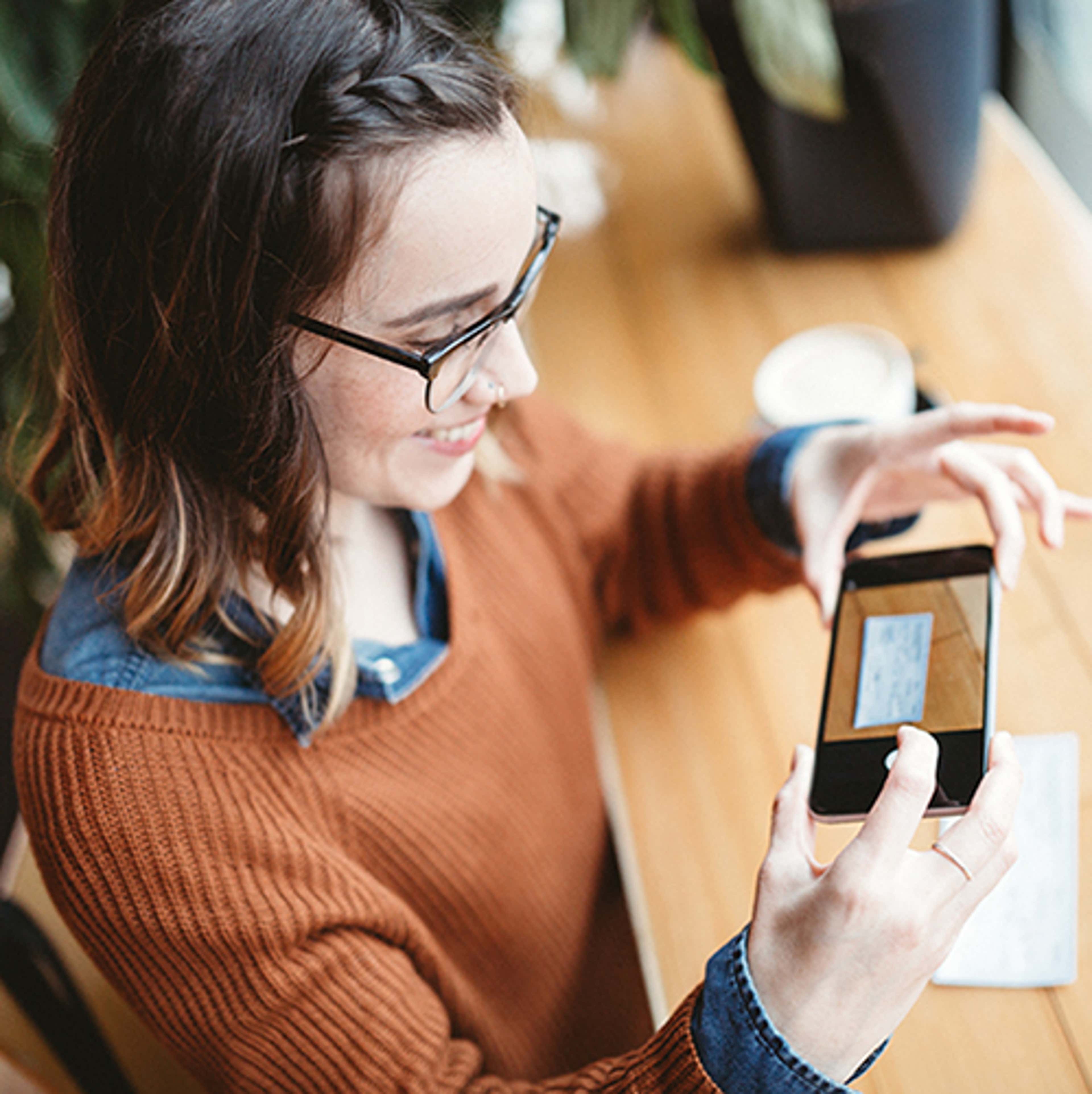 Young woman with glasses and brown hair taking a photo of cheque with a smartphone