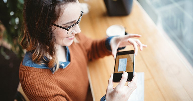 Young woman with glasses and brown hair taking a photo of a cheque with a smartphone