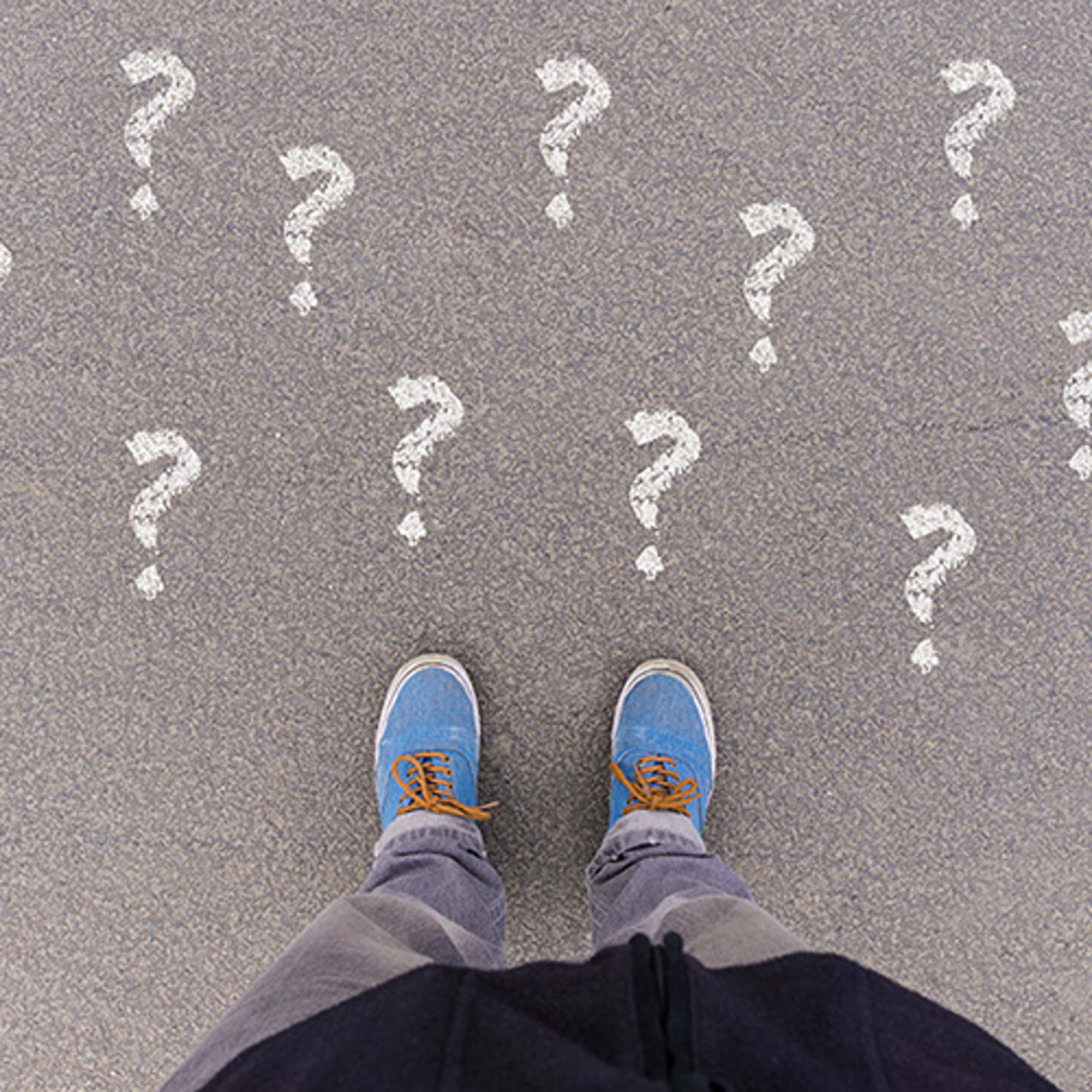 Person with blue shoes on pavement with question marks written in white chalk