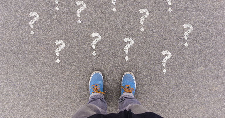 Feet on pavement with questions marks drawn in white chalk