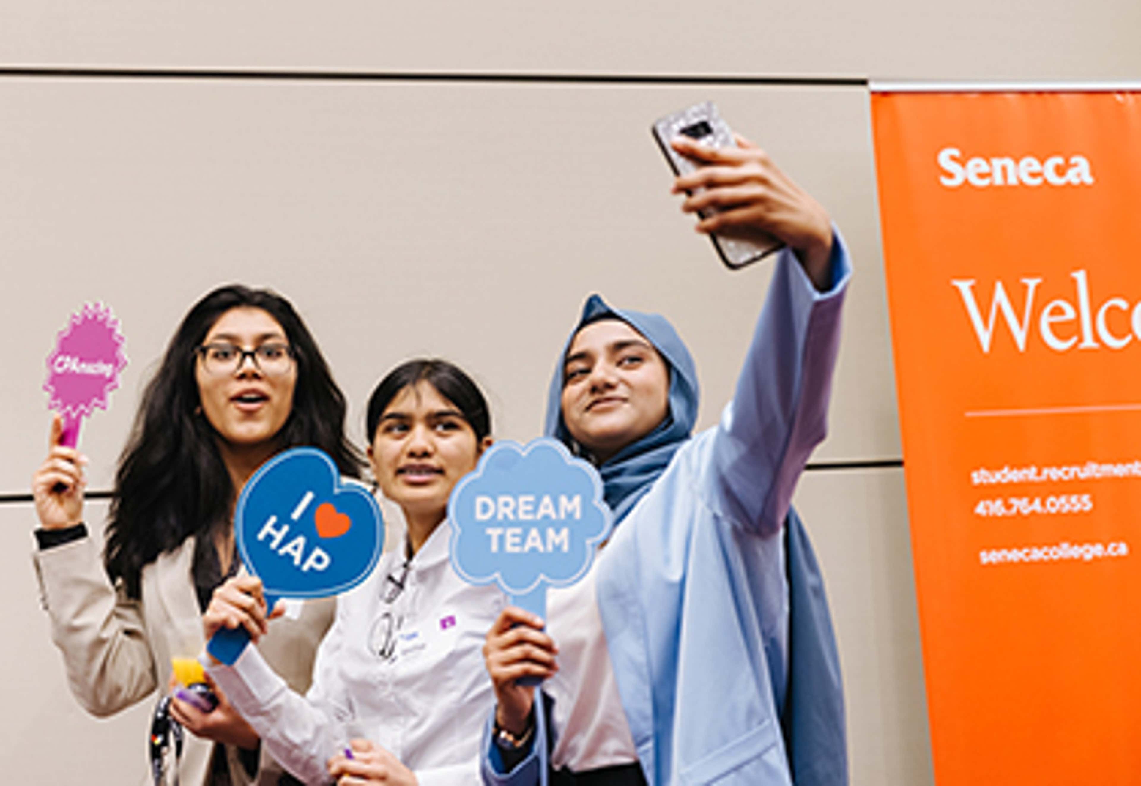 Three students taking selfies and holding CPA signs