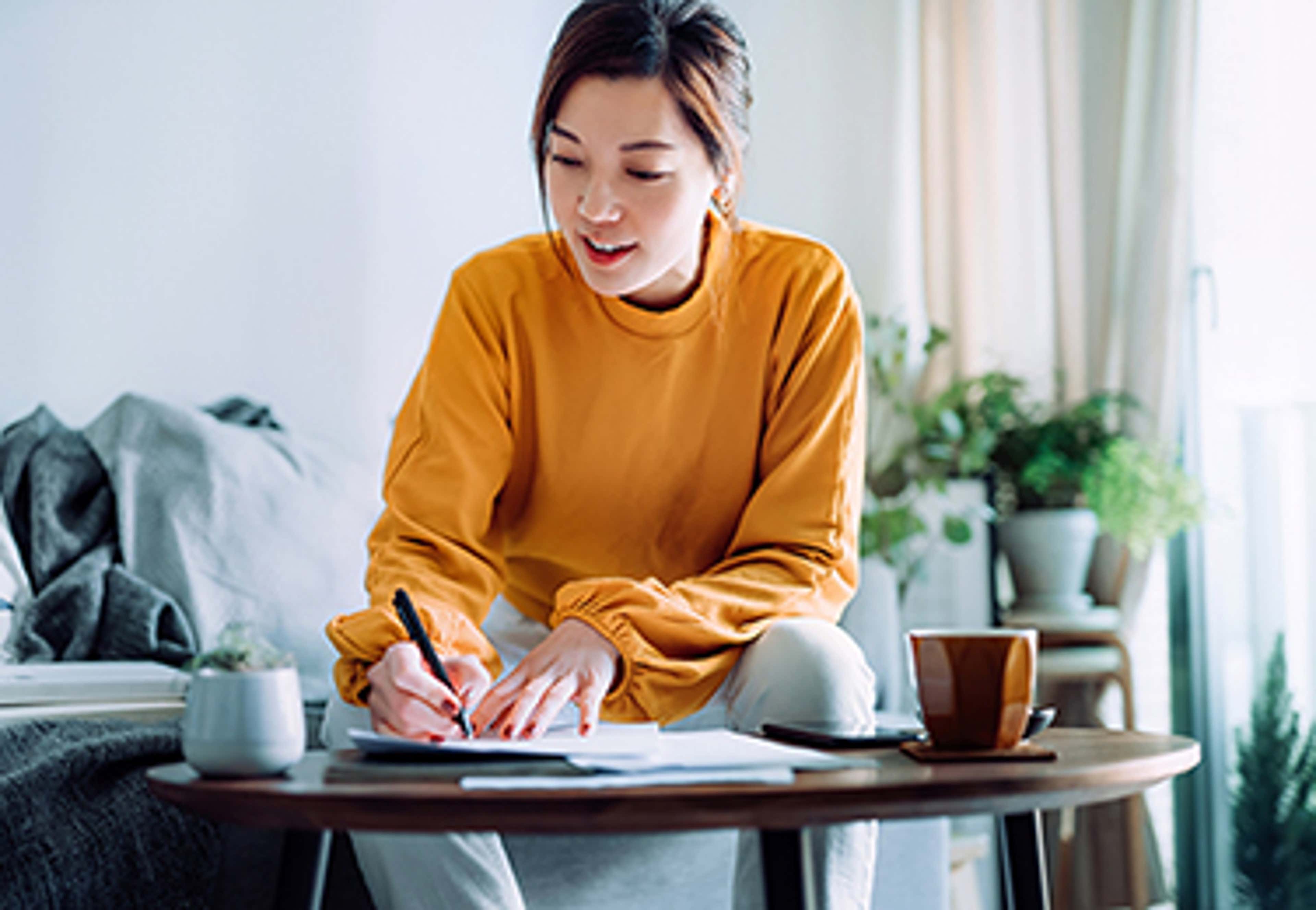 Woman in orange shirt writing at table