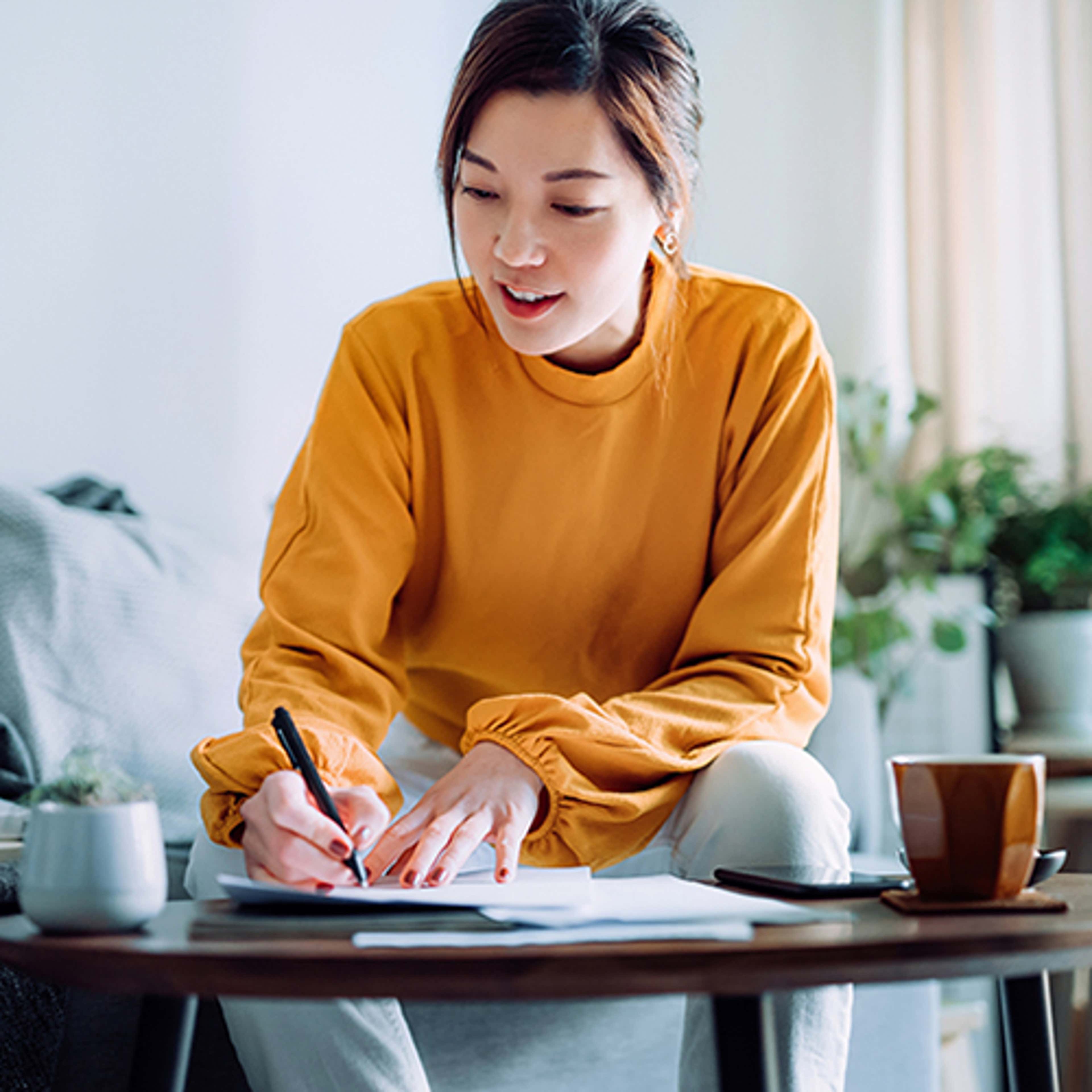 Woman in orange shirt writing at table