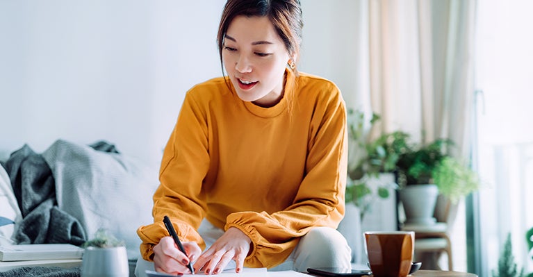 Woman in orange shirt writing at table