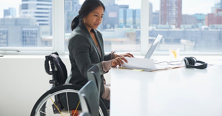 Woman in wheelchair sitting at a desk with a laptop