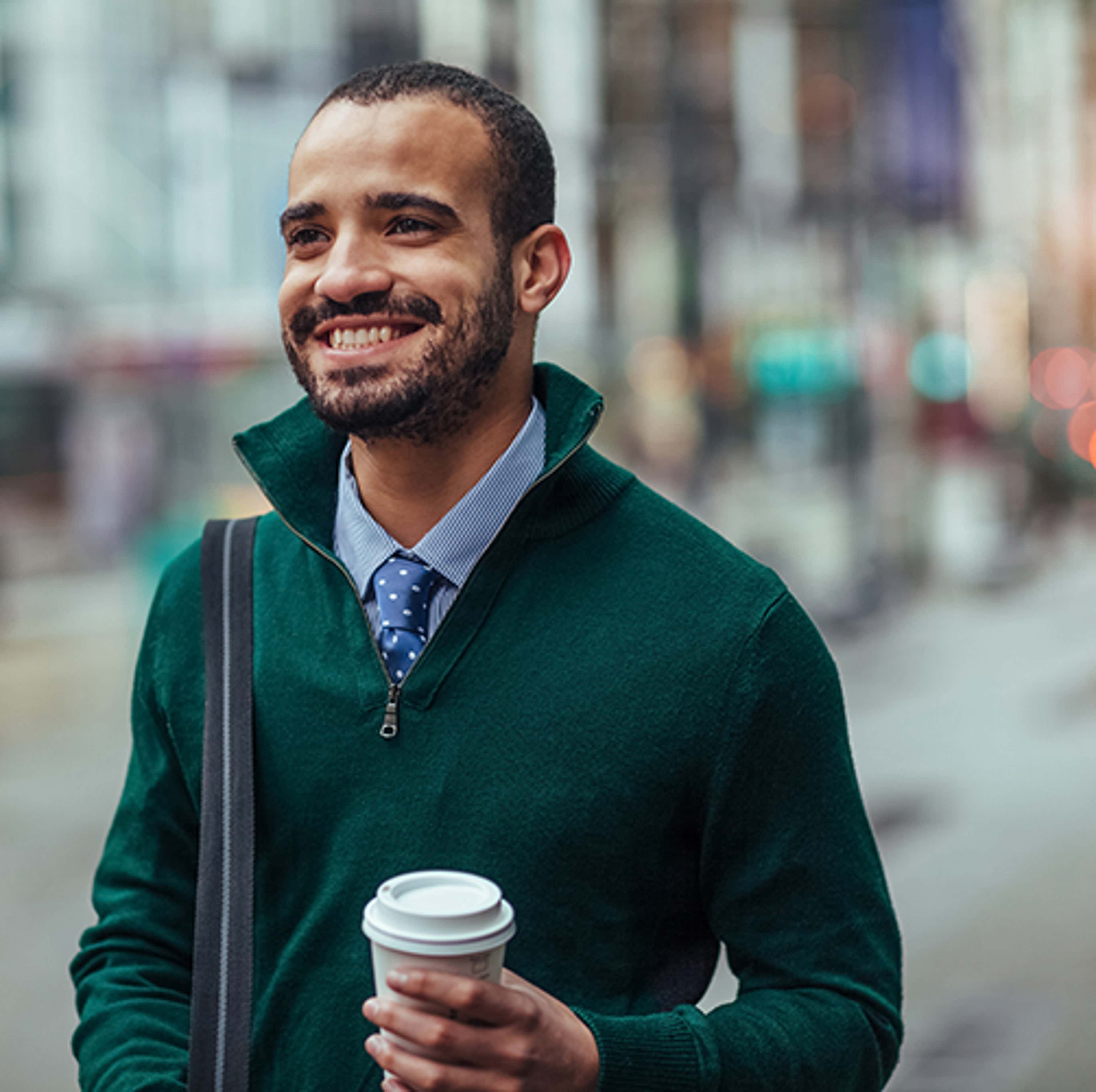 Man with green sweater, walking and smiling with coffee in hand