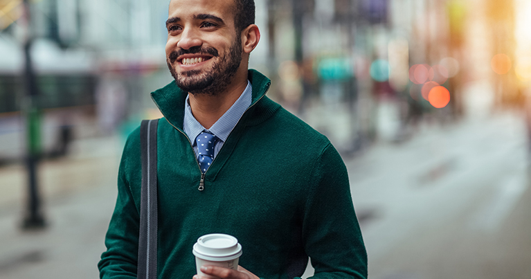 Man with green sweater, walking and smiling with coffee in hand