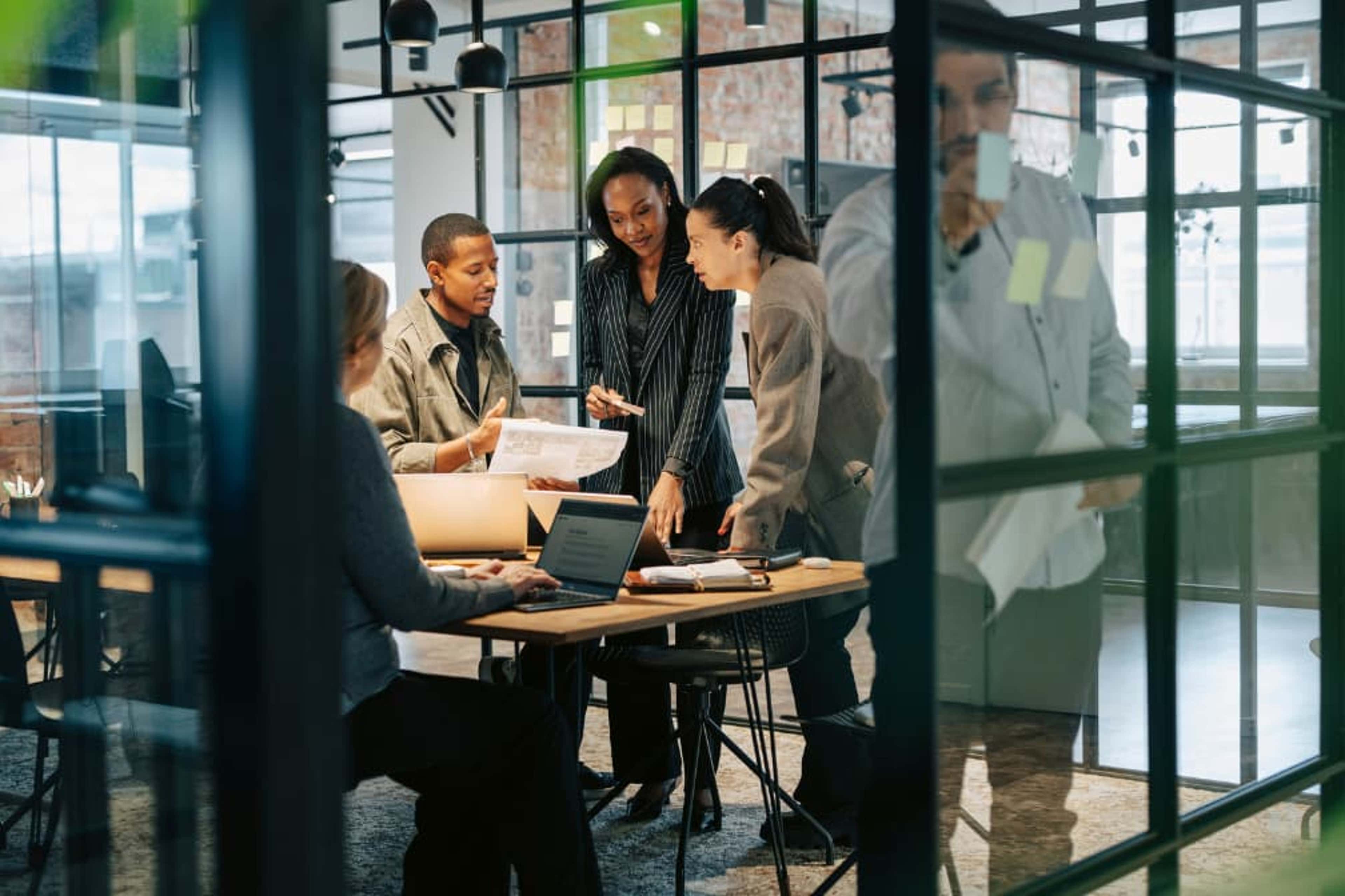 Team members engaged in discussion and teamwork at their office desks.