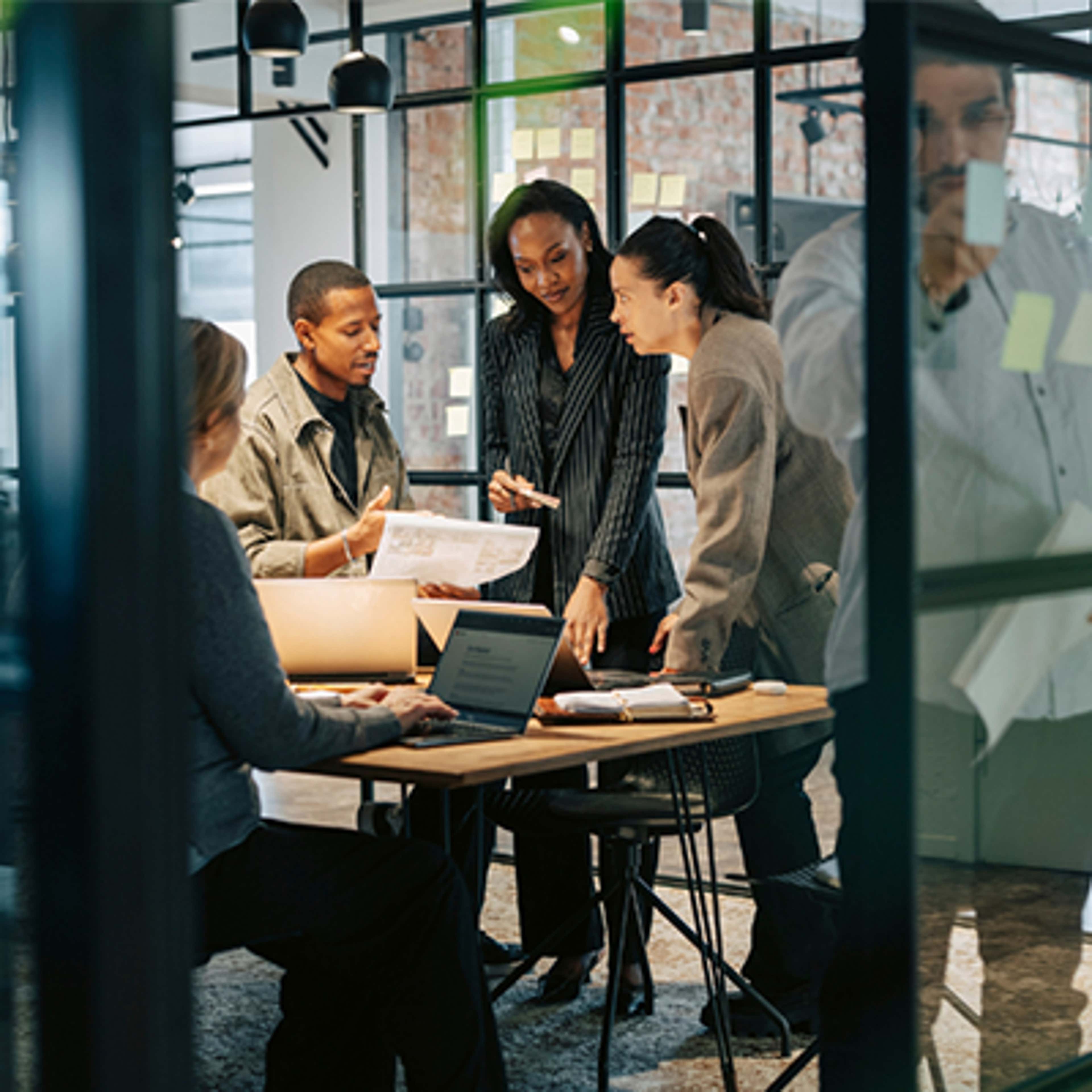 Team members engaged in discussion and teamwork at their office desks.