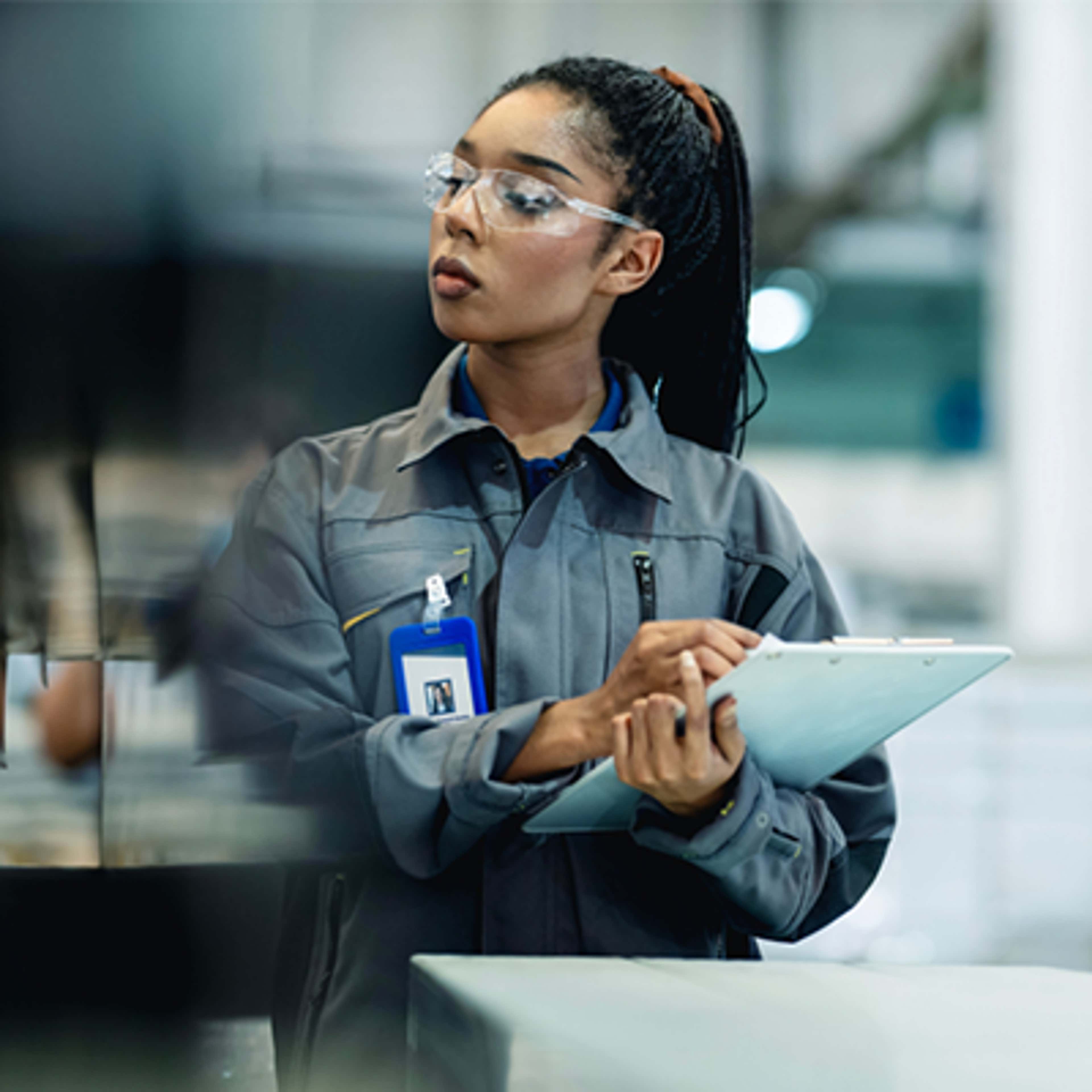 A woman in a factory writes on a clipboard