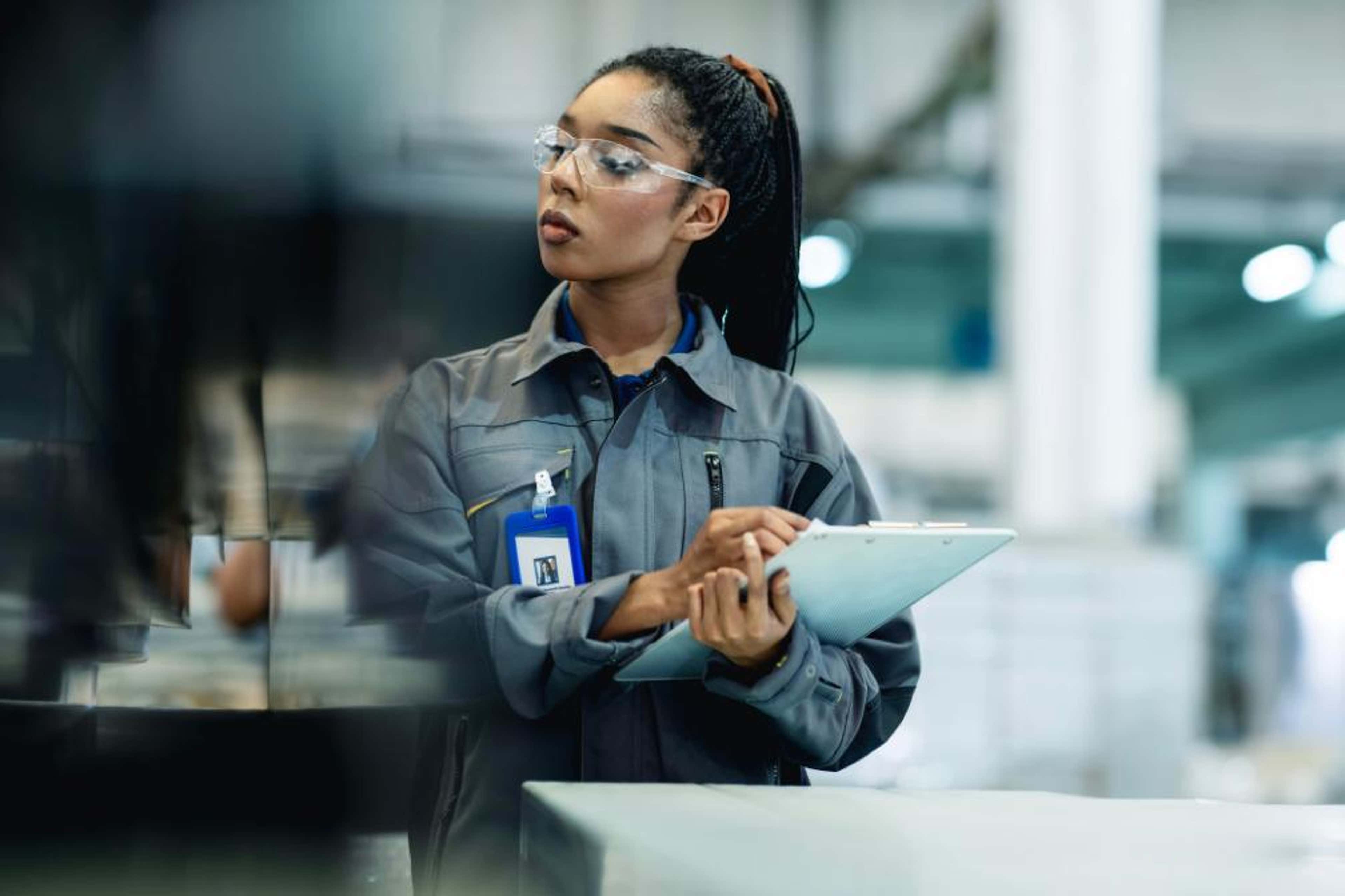A woman in a factory writes on a clipboard