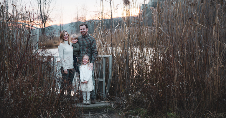 Ewa and Danny's family standing in front of a pond surrounded by tall grasses