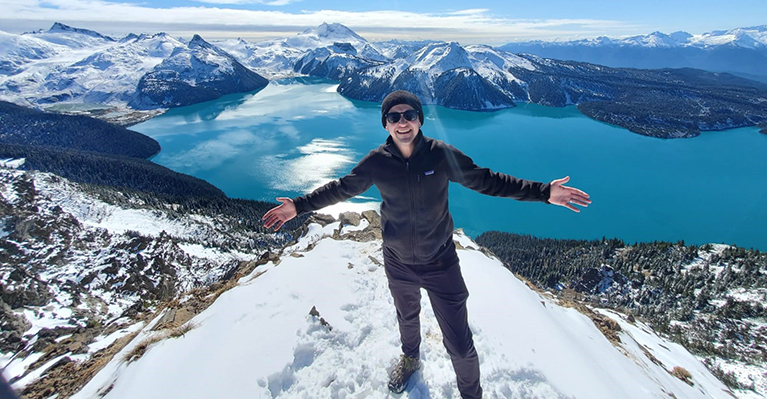 Michael on a snow-capped mountain overlooking a lake and mountains