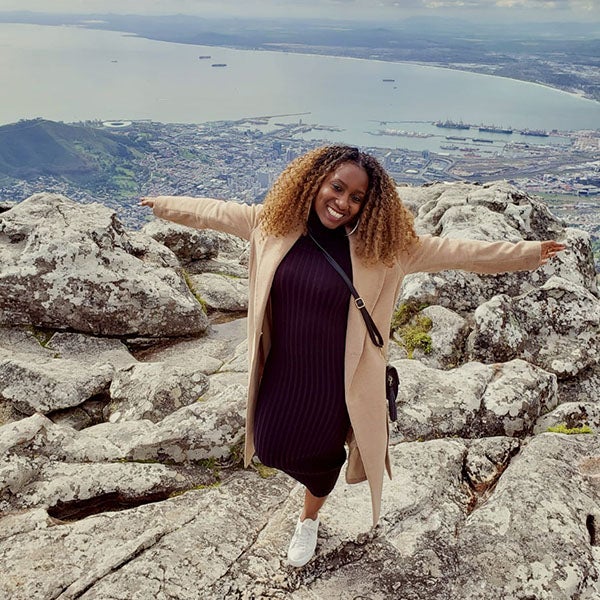 Vivienne Lutwama standing on a rocky peak in front of water