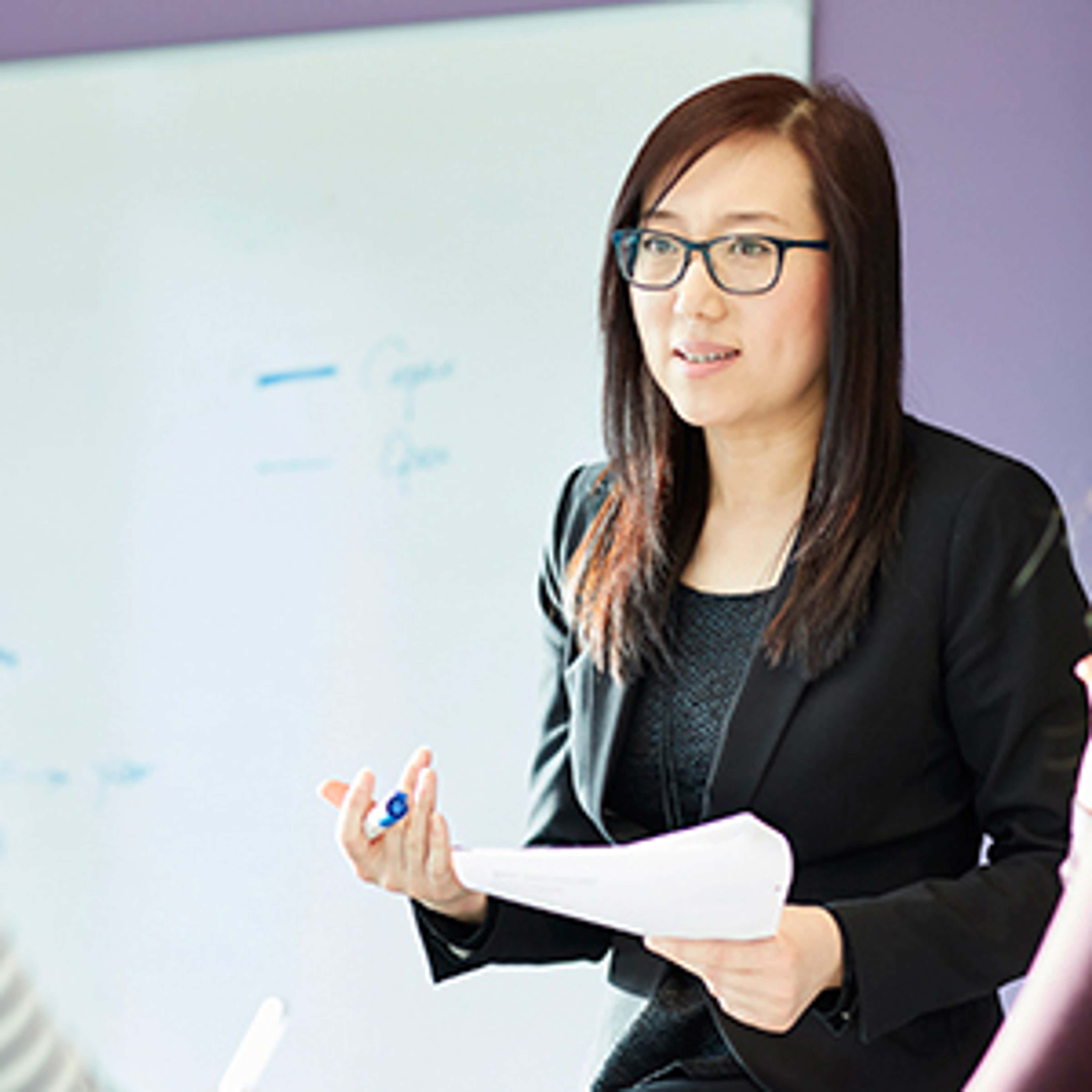 Woman with glasses in suit standing and speaking