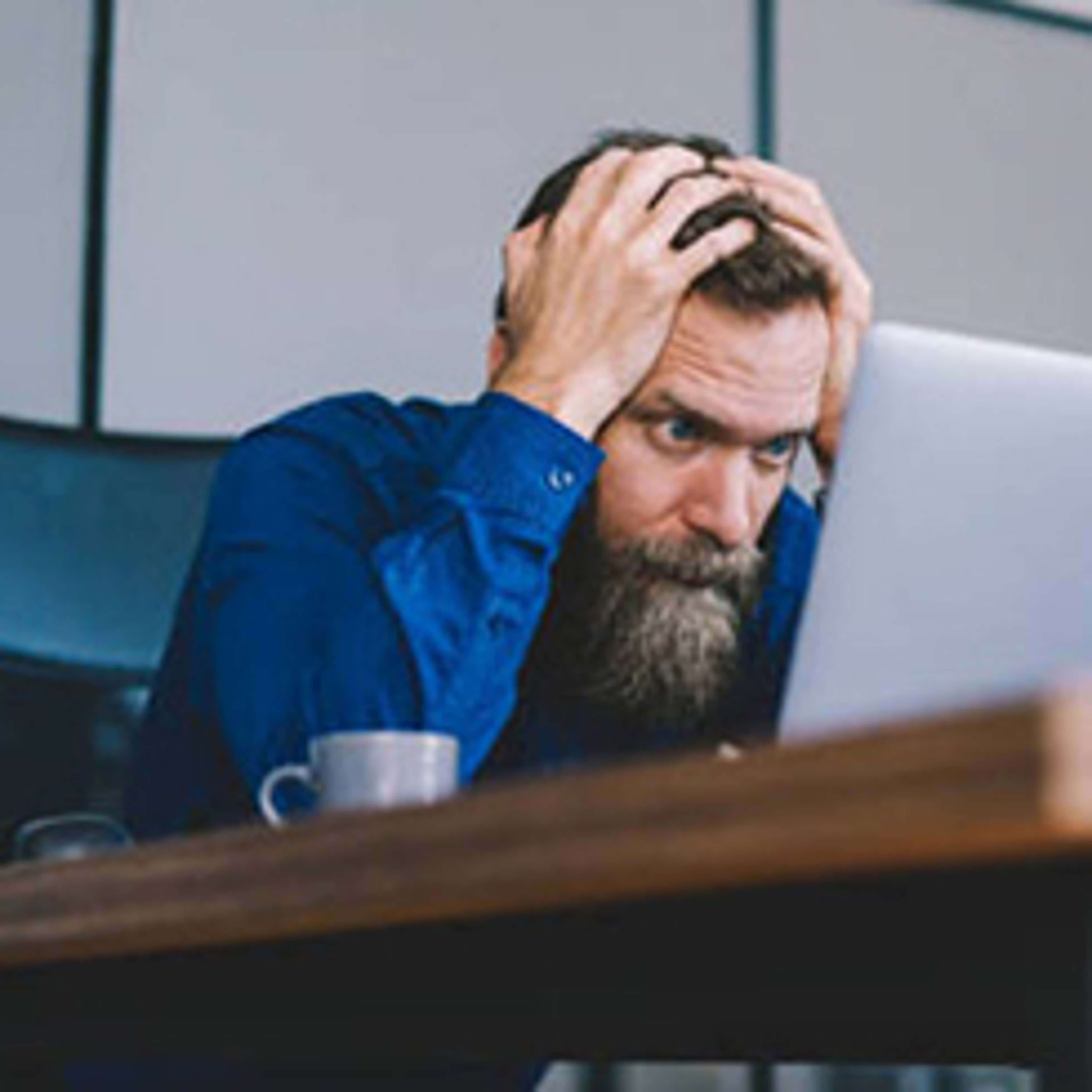 Person holding head in hands looking at laptop