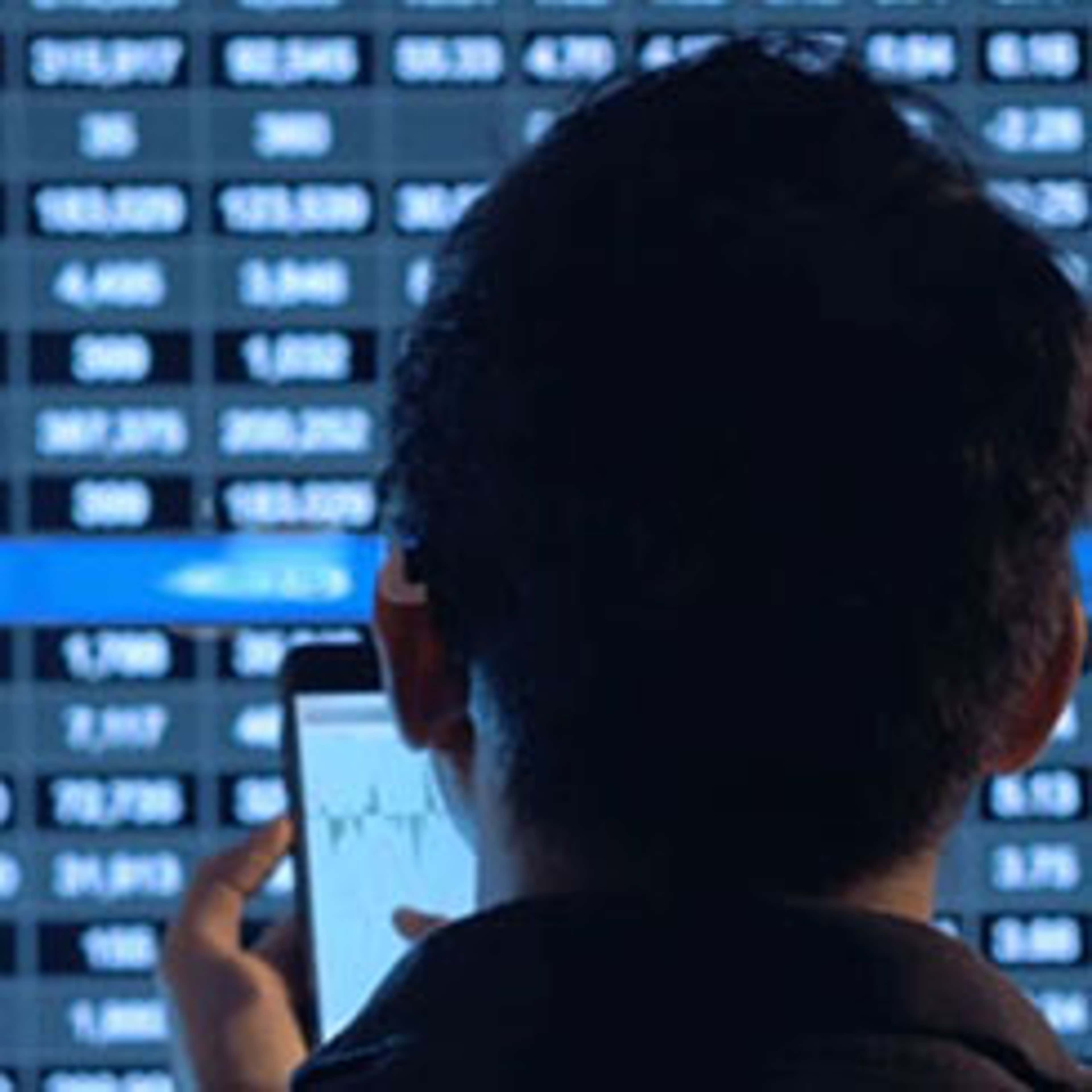 Person looking at stock market screen and cellphone