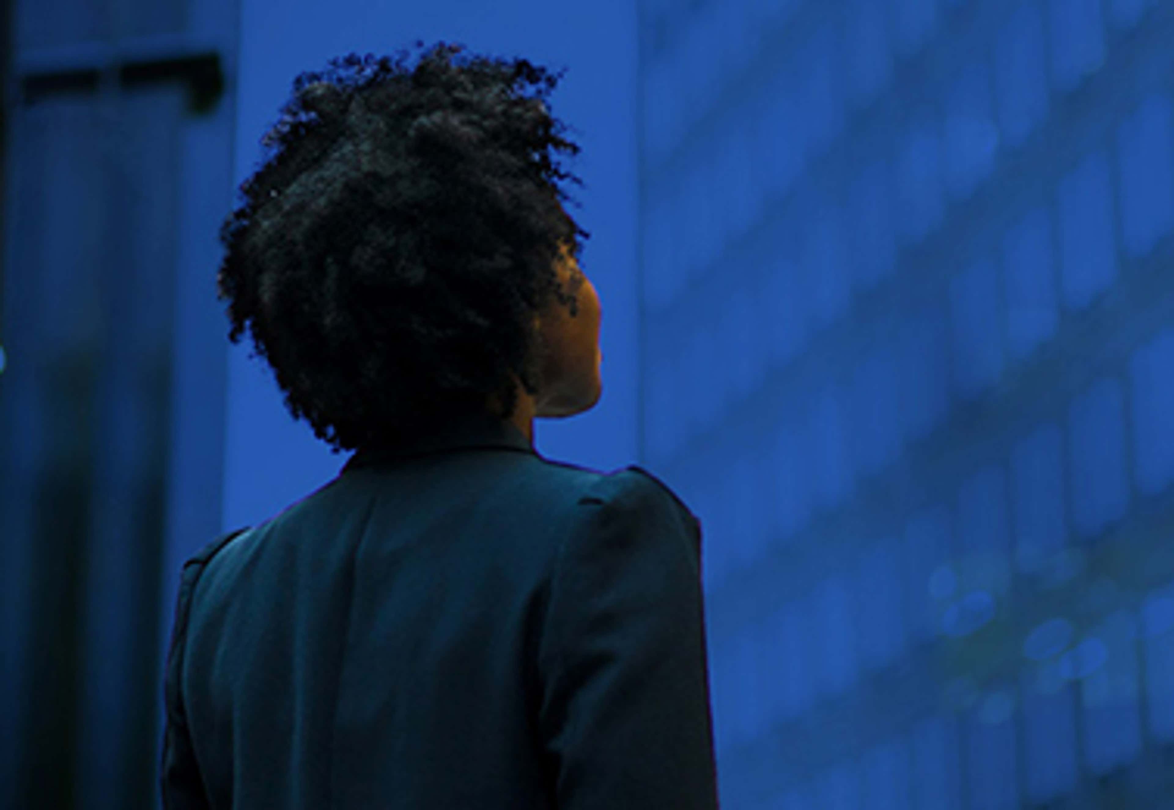 Woman looking up at dark blue sky surrounded by skyscrapers
