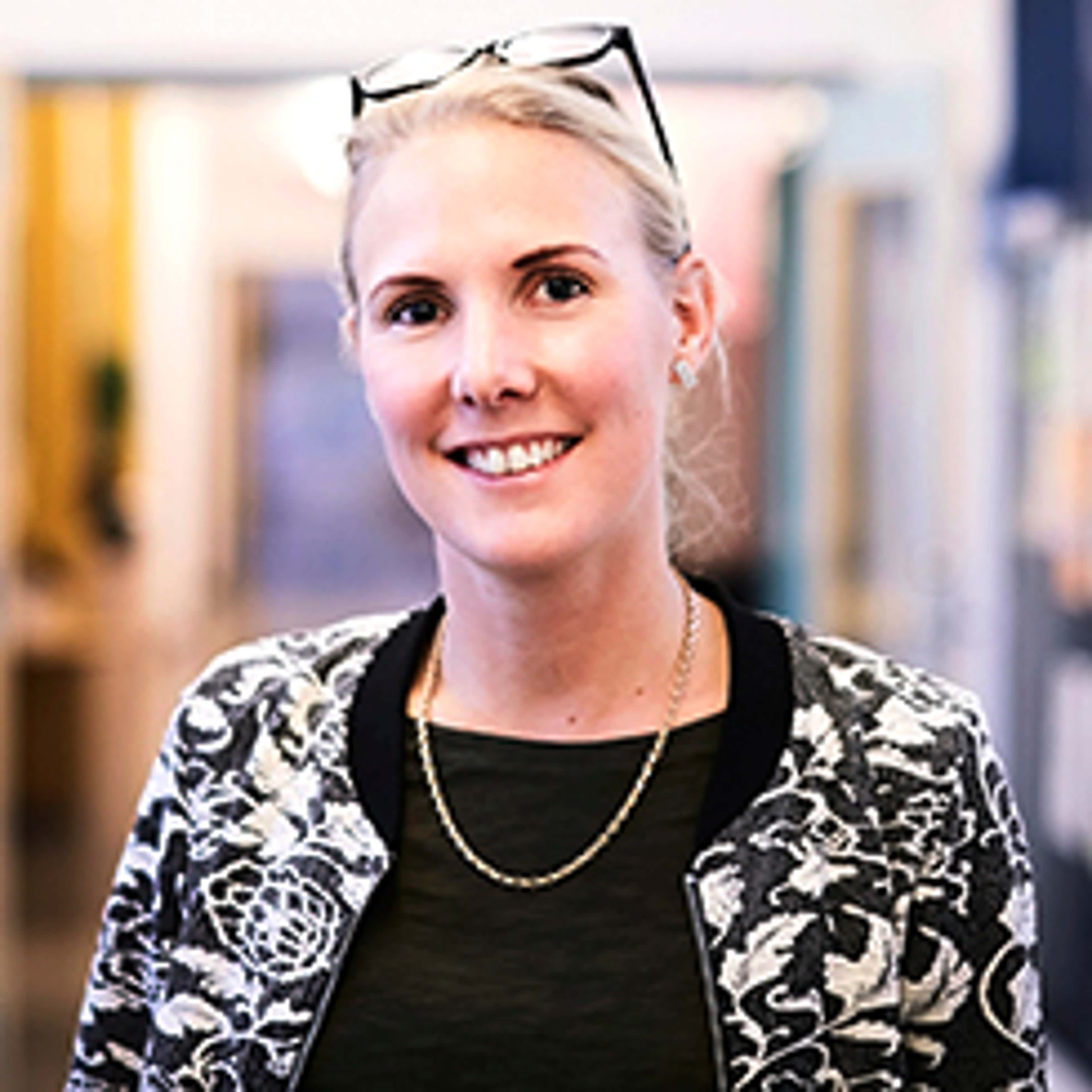 Woman with spectacles over her head, wearing a black top and black and white jacket, smiling at the camera