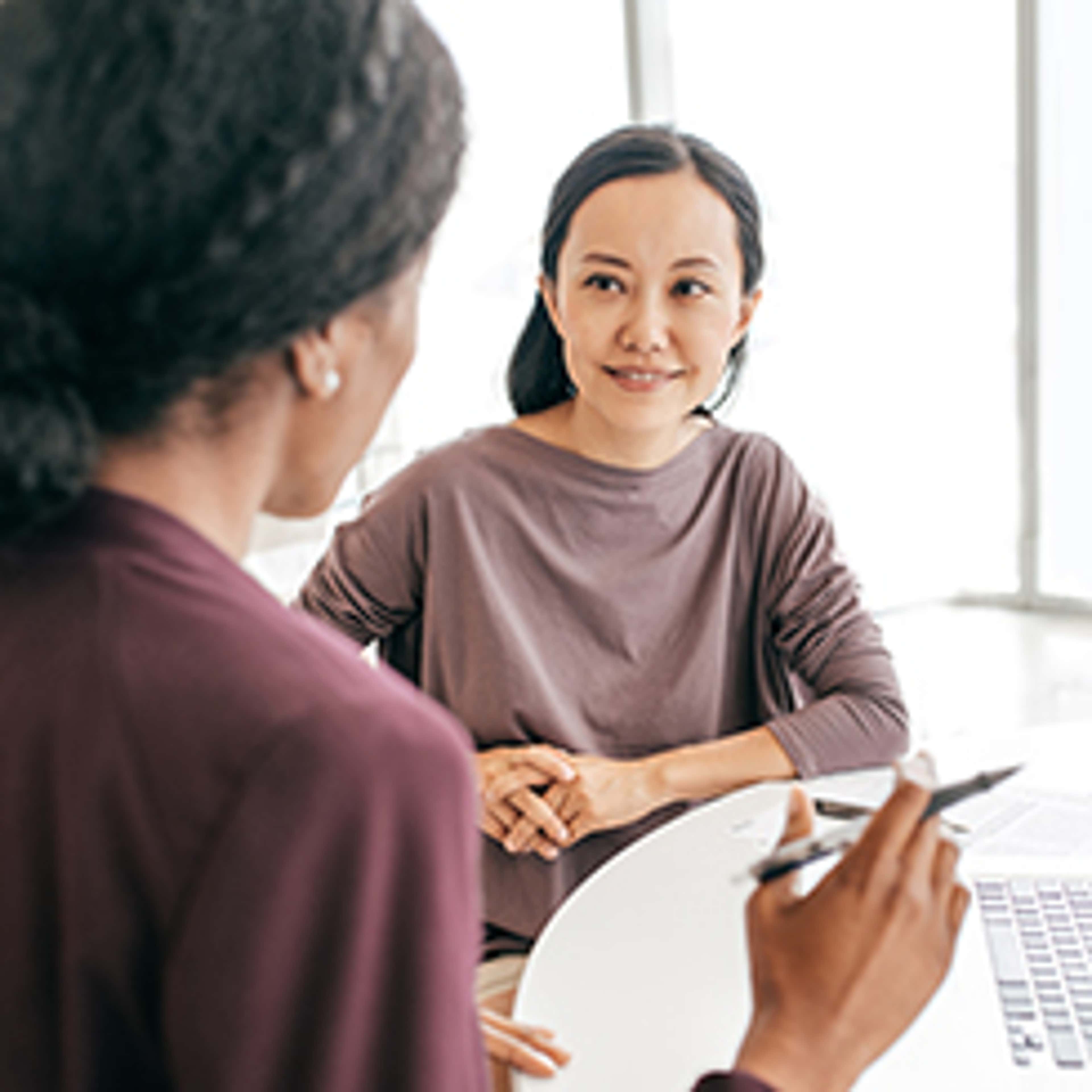 Two women talking at desk, one with pen in hand