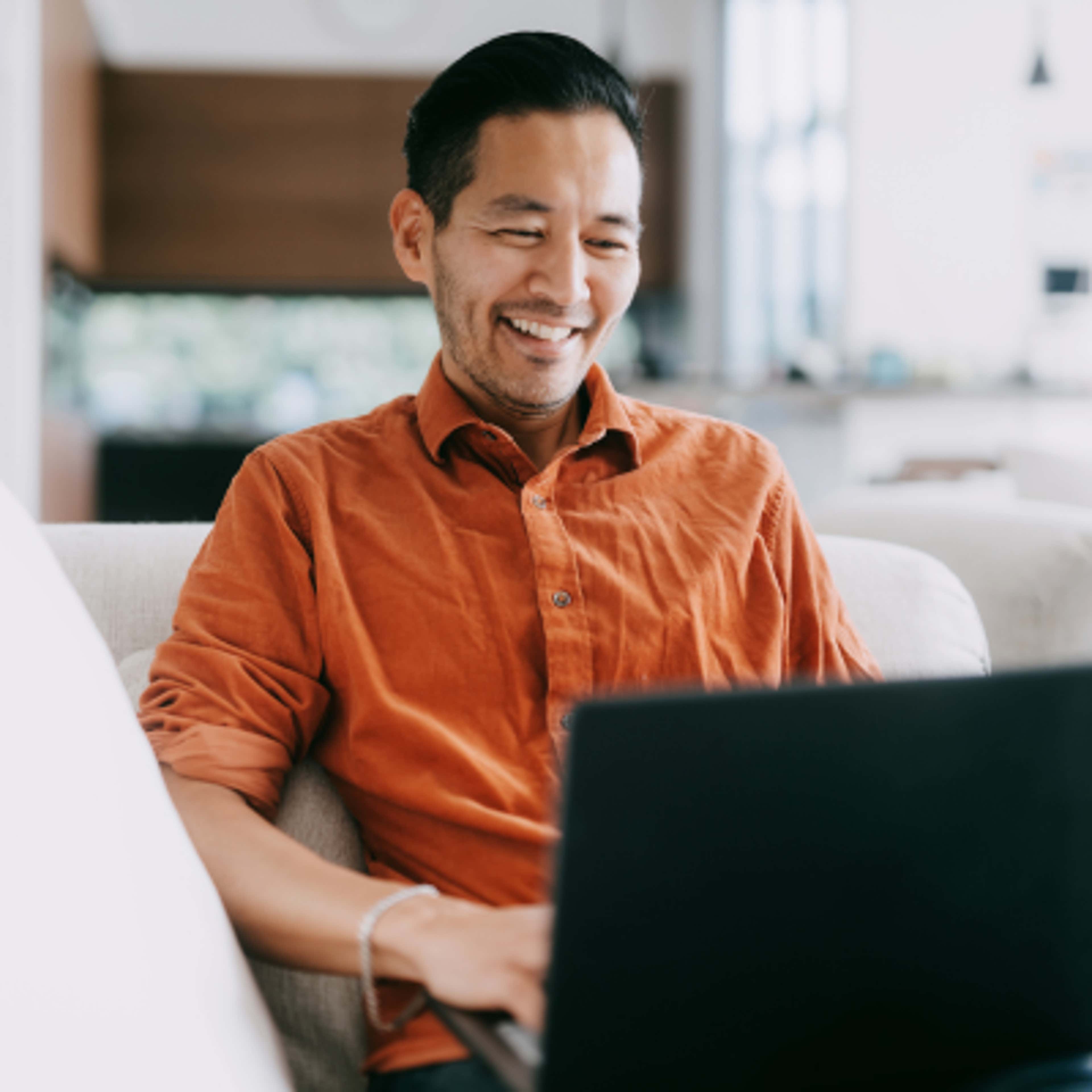 A man sitting with Laptop in Orange Shirt