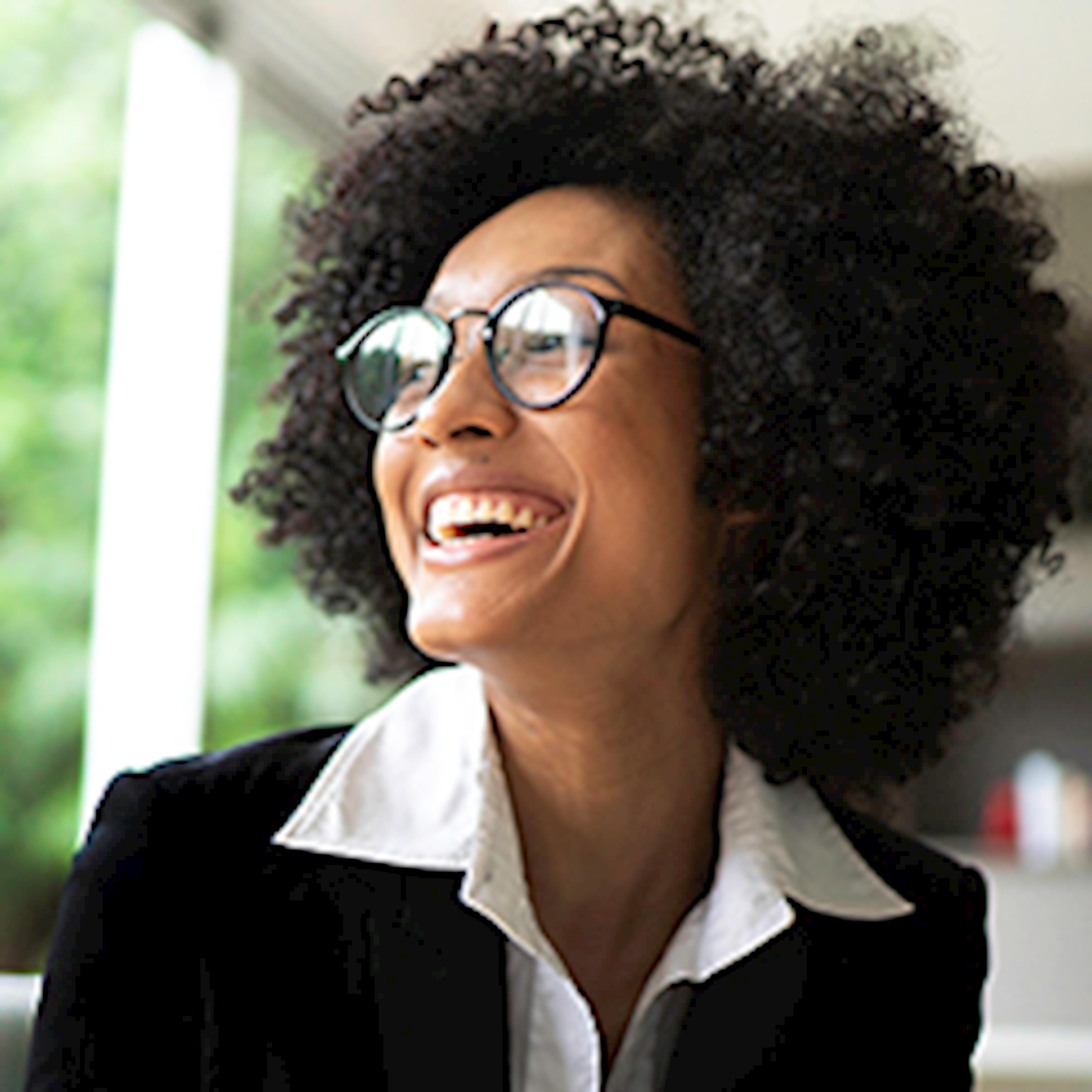 Woman with dark hair, suit and glasses laughing