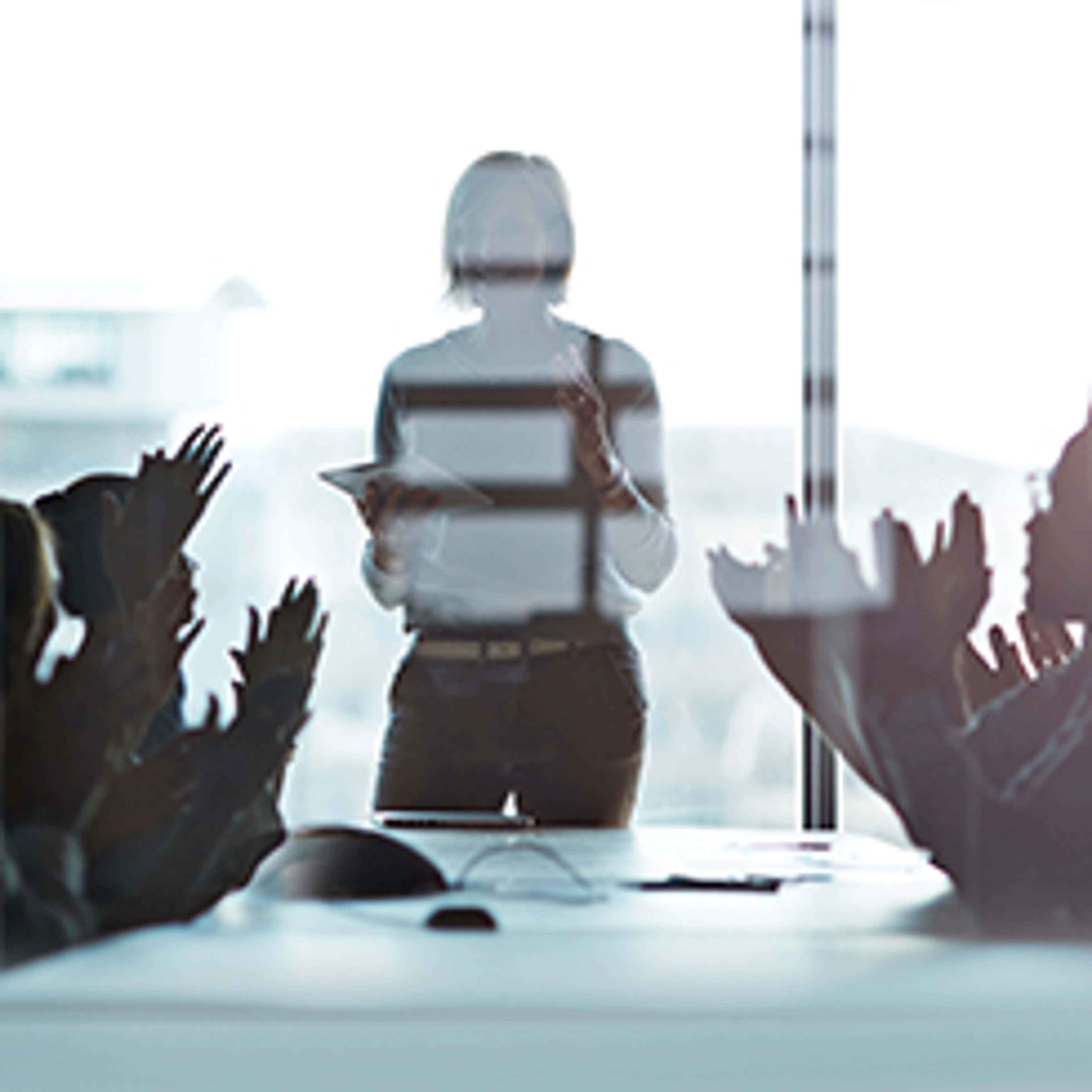 Woman standing and talking in front of a window with people sitting and clapping