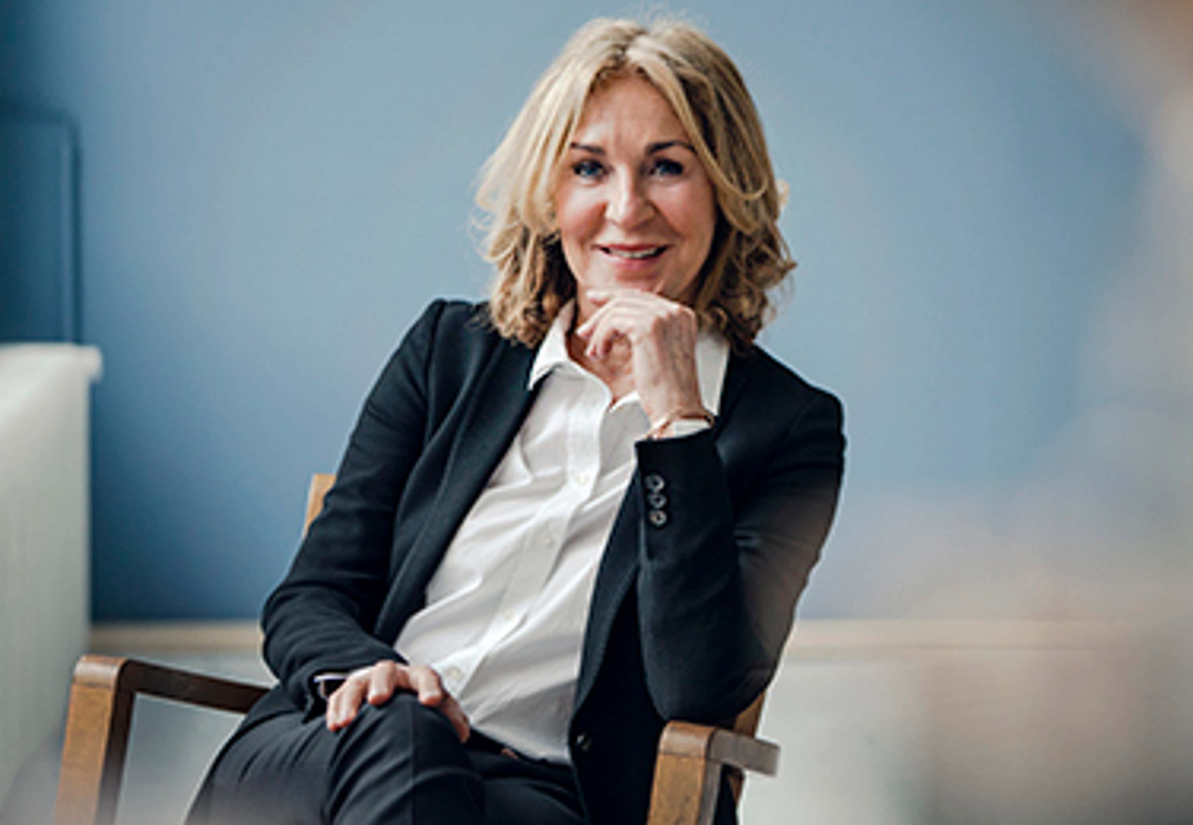 Woman in white shirt, formal suit, sitting in chair, smiling at camera