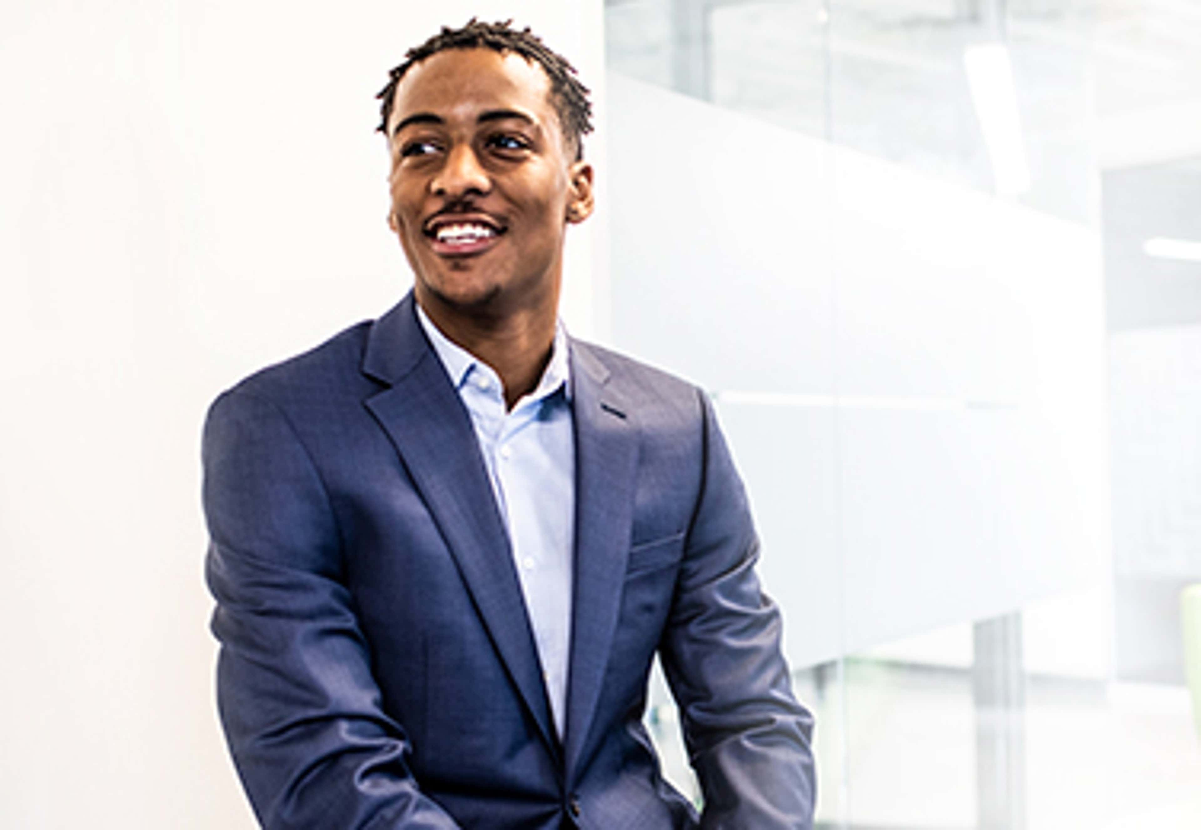Young man wearing navy blue formal suit sitting in front of white background