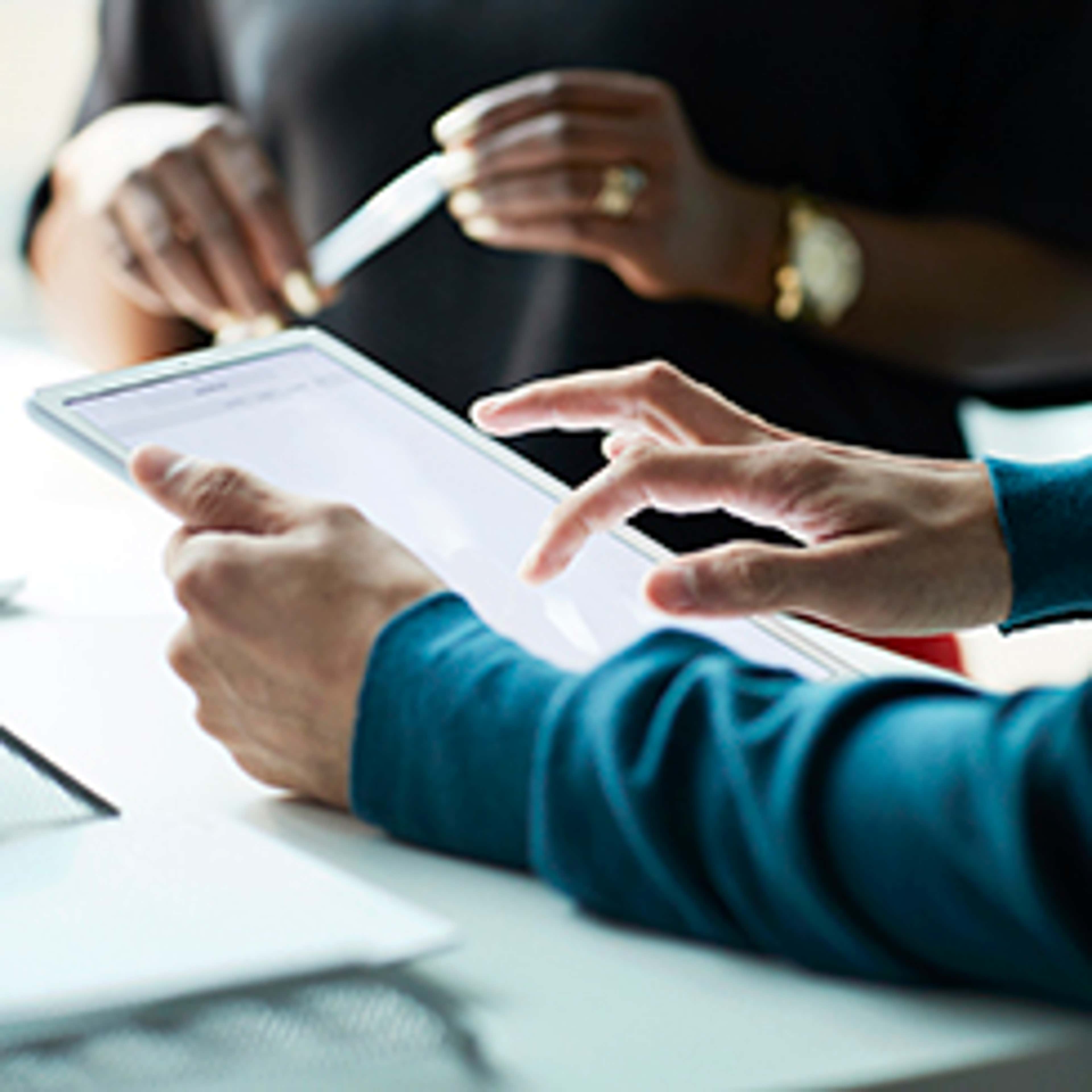 Close up of hands working on tablet, while other set of hands holds a pen
