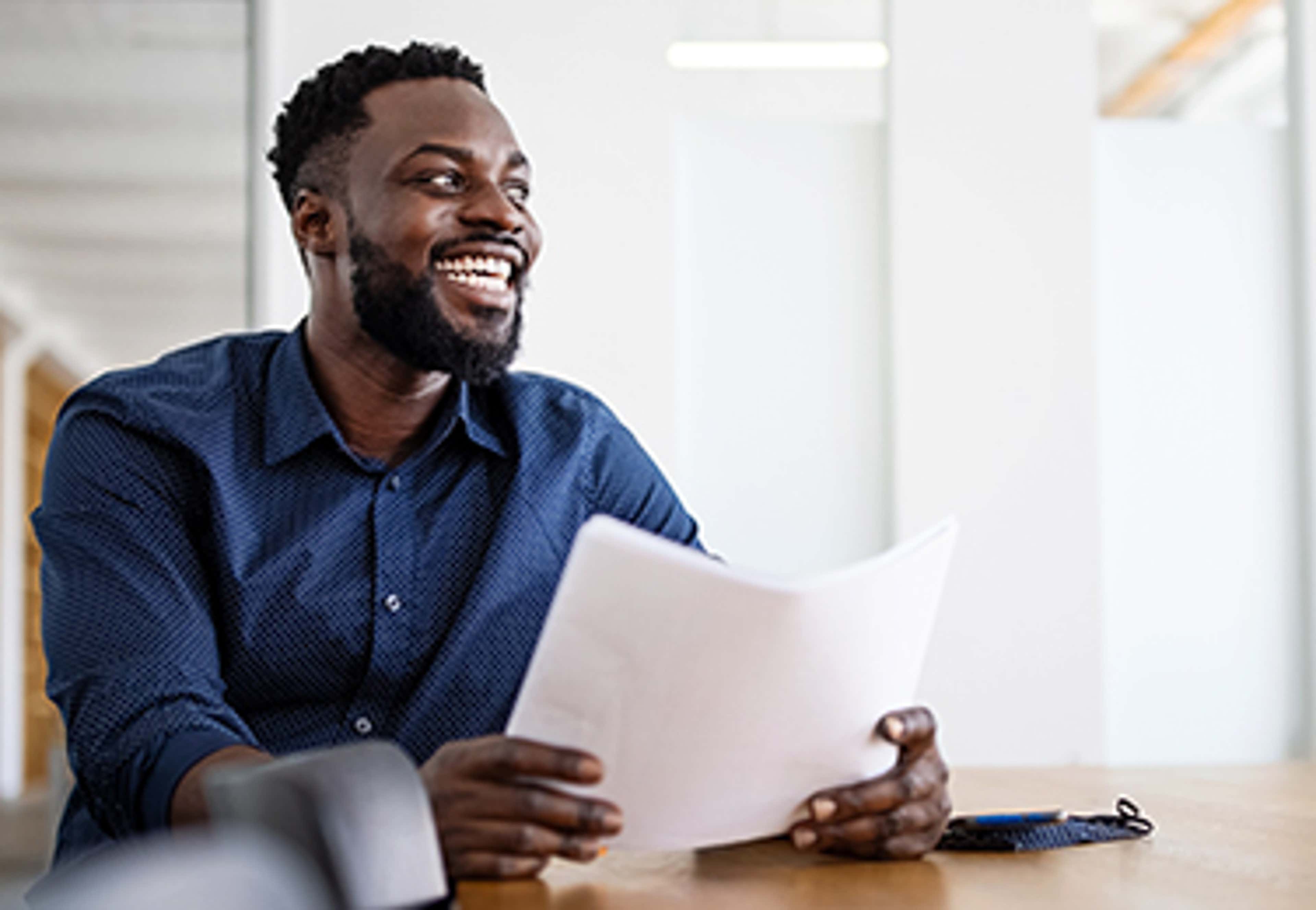 Man in blue shirt smiling at someone outside picture while holding papers