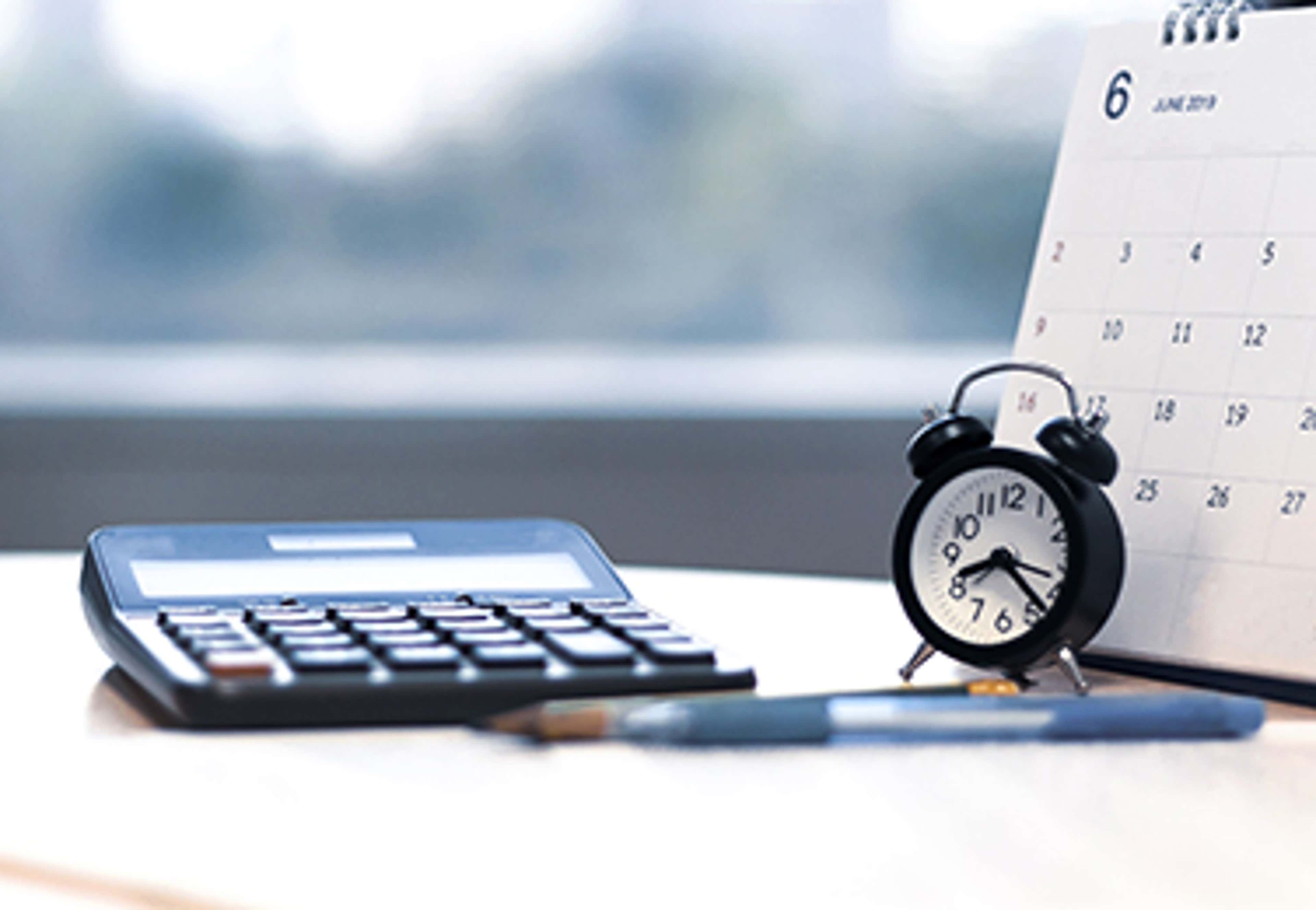 Calculator, alarm clock and calendar on a table overlooking a trees outside