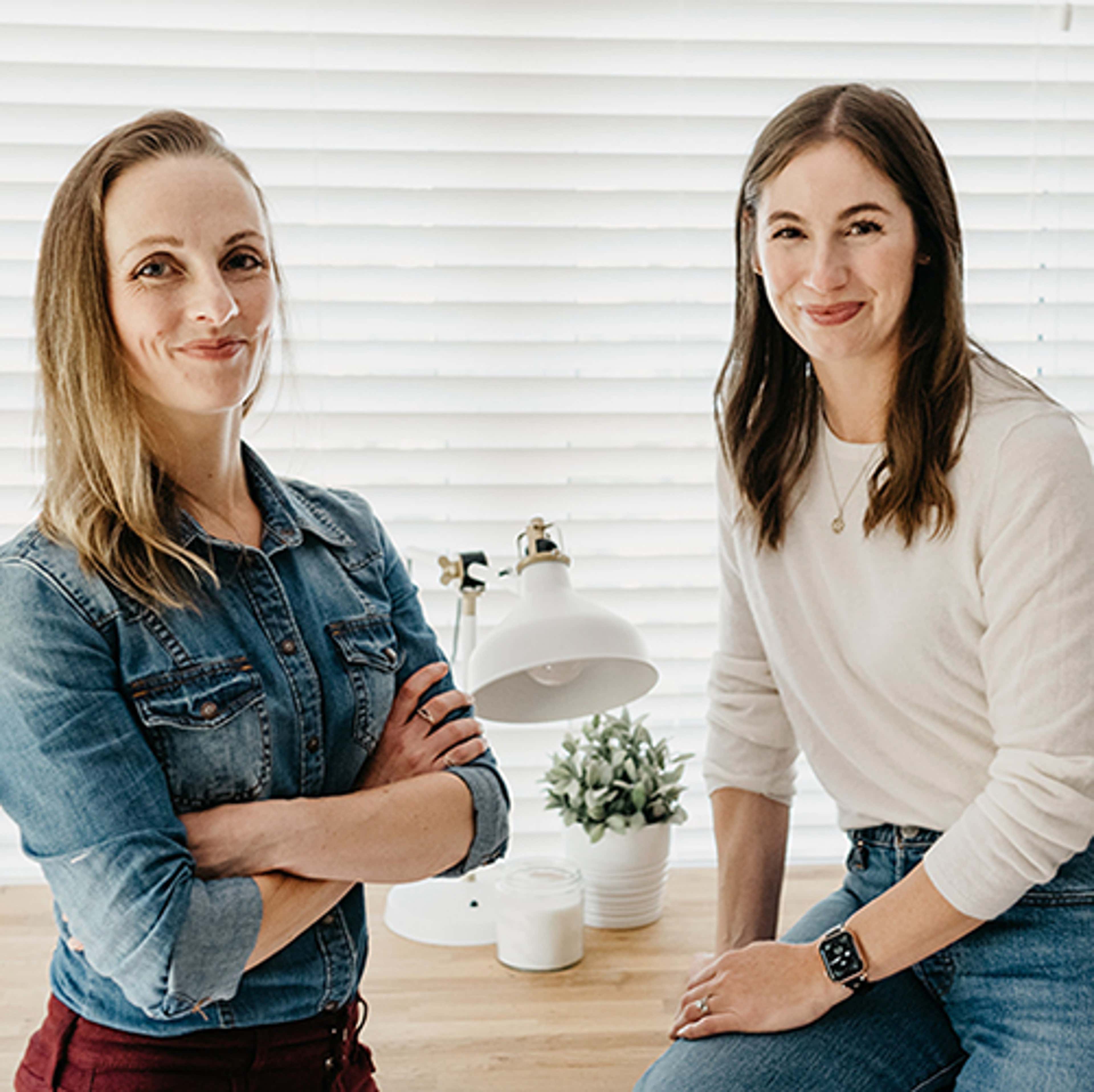 Two women standing in front of closed window, smiling at camera